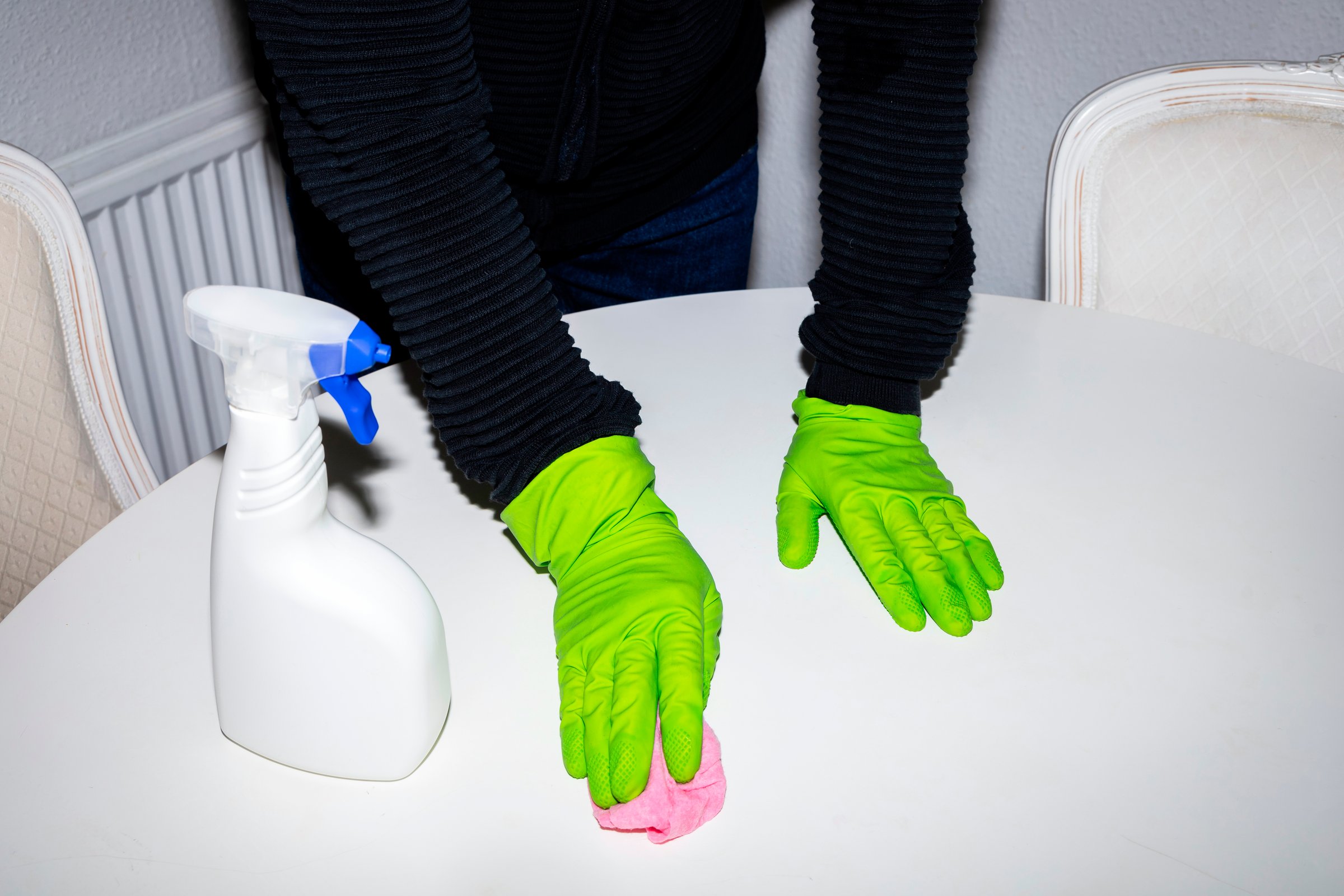A person in rubber gloves cleaning the dining table and using cloth and disinfectant spray, detergent. House cleaning and hygiene concept.