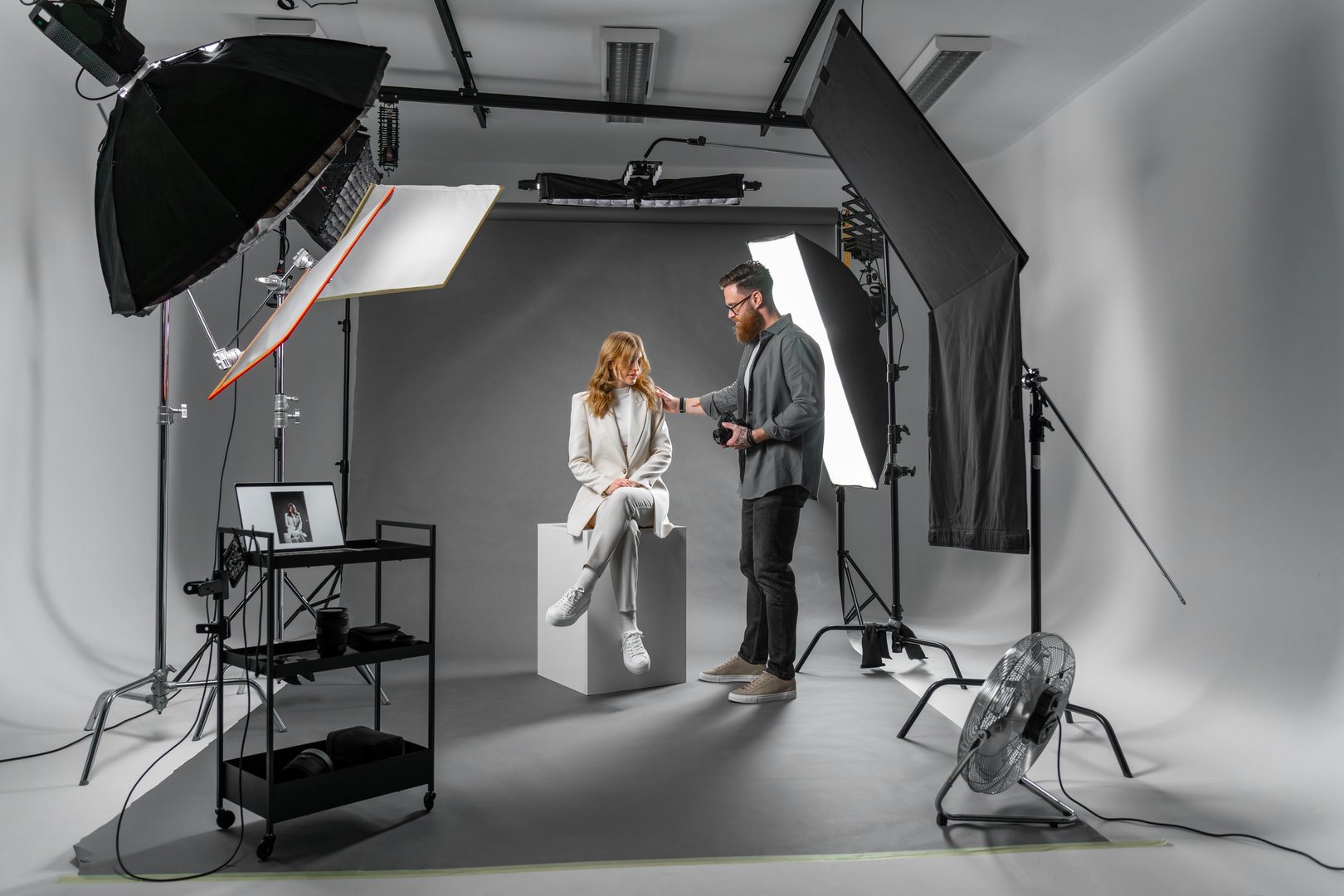 Professional photographer and beautiful model on fashion shoot in photo studio with lighting equipment. Occupation concept