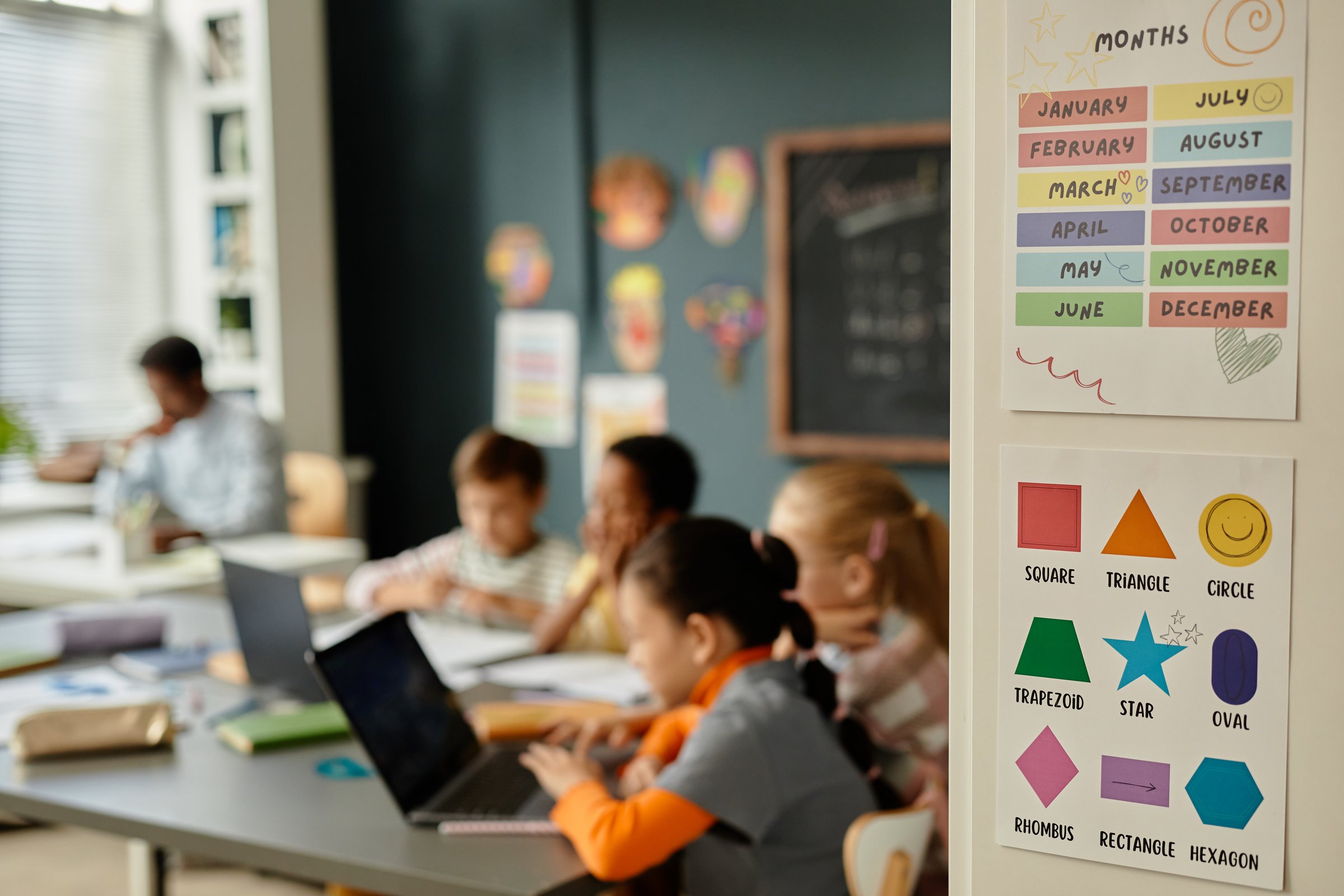 Background shot of educational posters on cupboard with colorful pictures of months of year and different geometric shapes in primary school classroom
