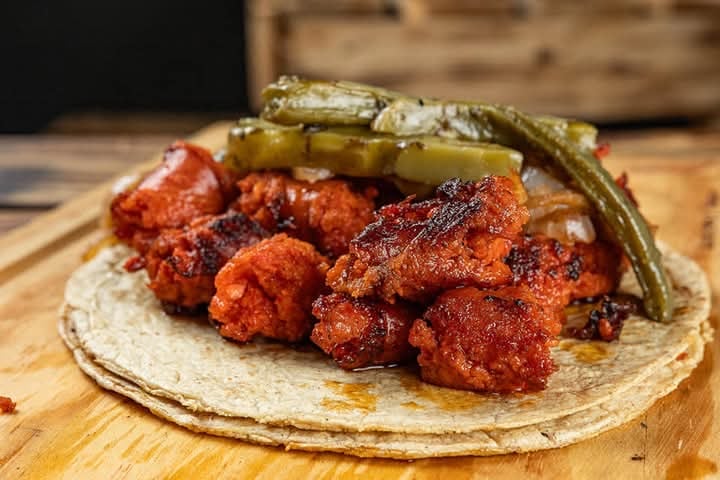 Taco with spicy marinated meat and grilled green peppers on a wooden board.