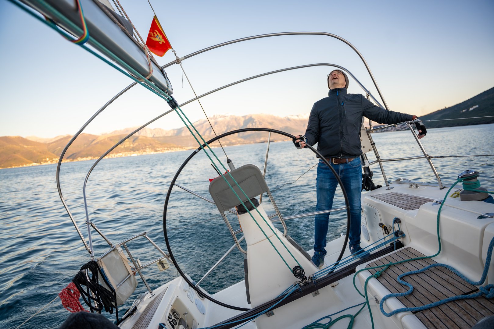 Young man captain standing at the helm and controls a sailboat during a journey by sea in winter time in Montenegro. High quality photo