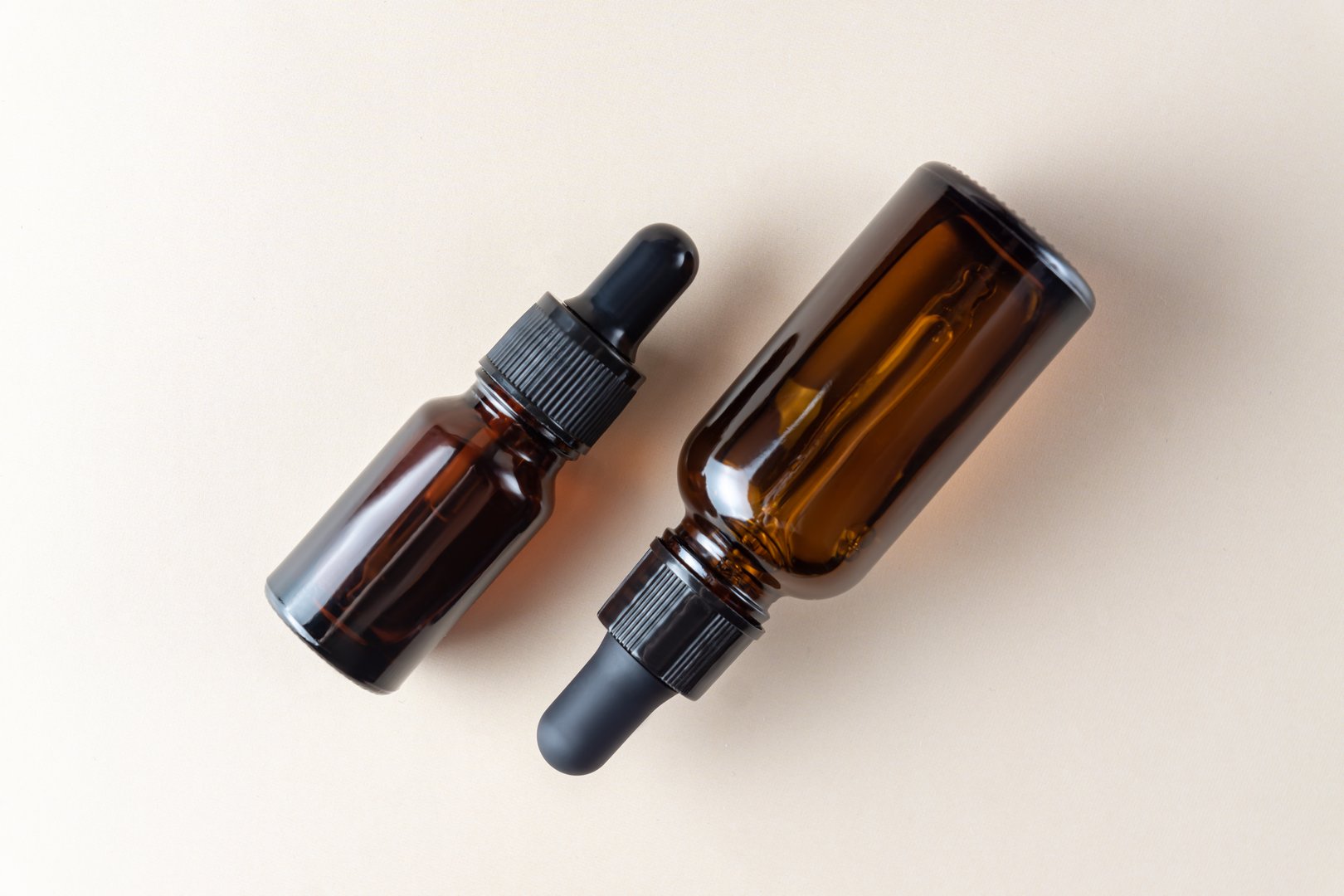 Cosmetic oil in glass bottles with dropper on beige background. Beauty wellness concept. Top view, copy space.