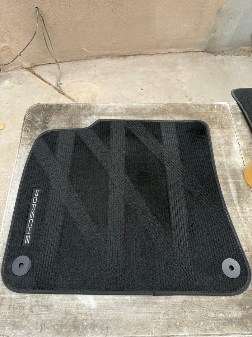 Black car floor mat with Porsche logo, placed on a concrete surface.