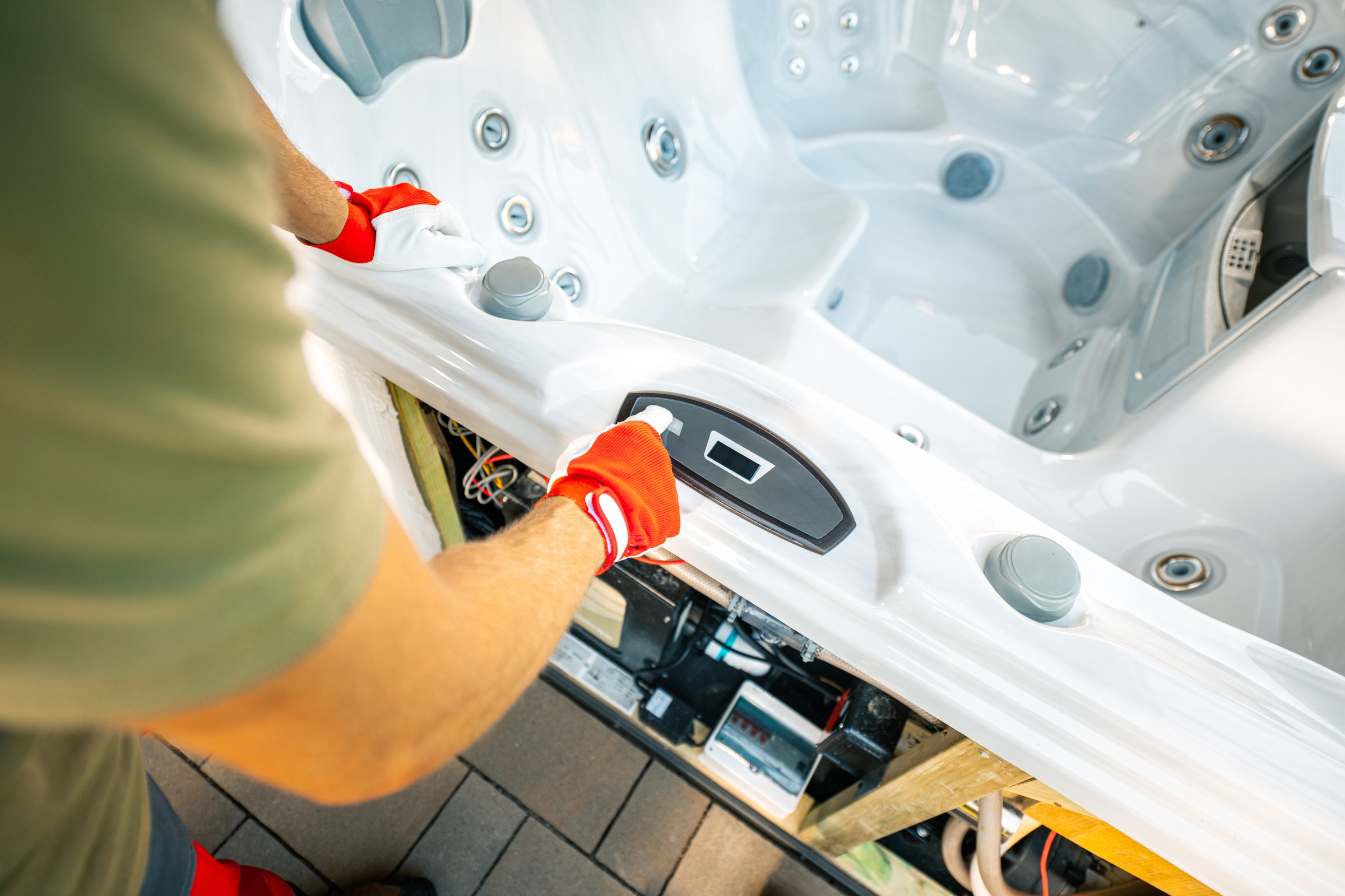 A technician in gloves is adjusting the control panel of a hot tub, ensuring proper functionality while surrounded by the tub's interior features.