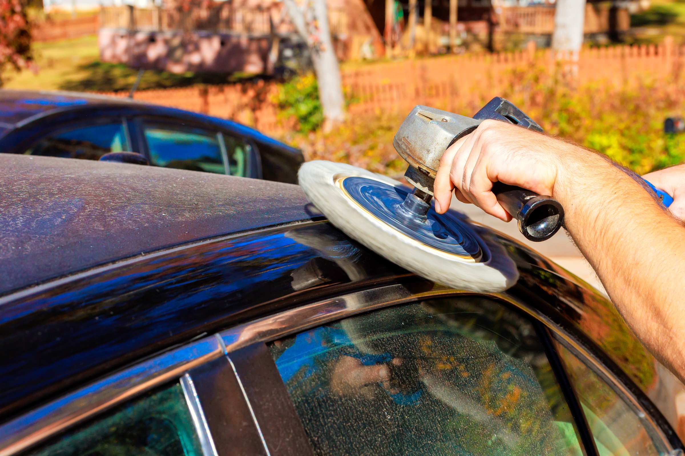 Technician worker is using buffing tool to polish top of dusty car in car service garage