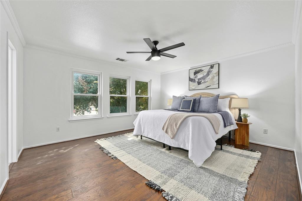 Spacious bedroom with a large bed, pillows, and a throw blanket, ceiling fan, windows, and hardwood floors.