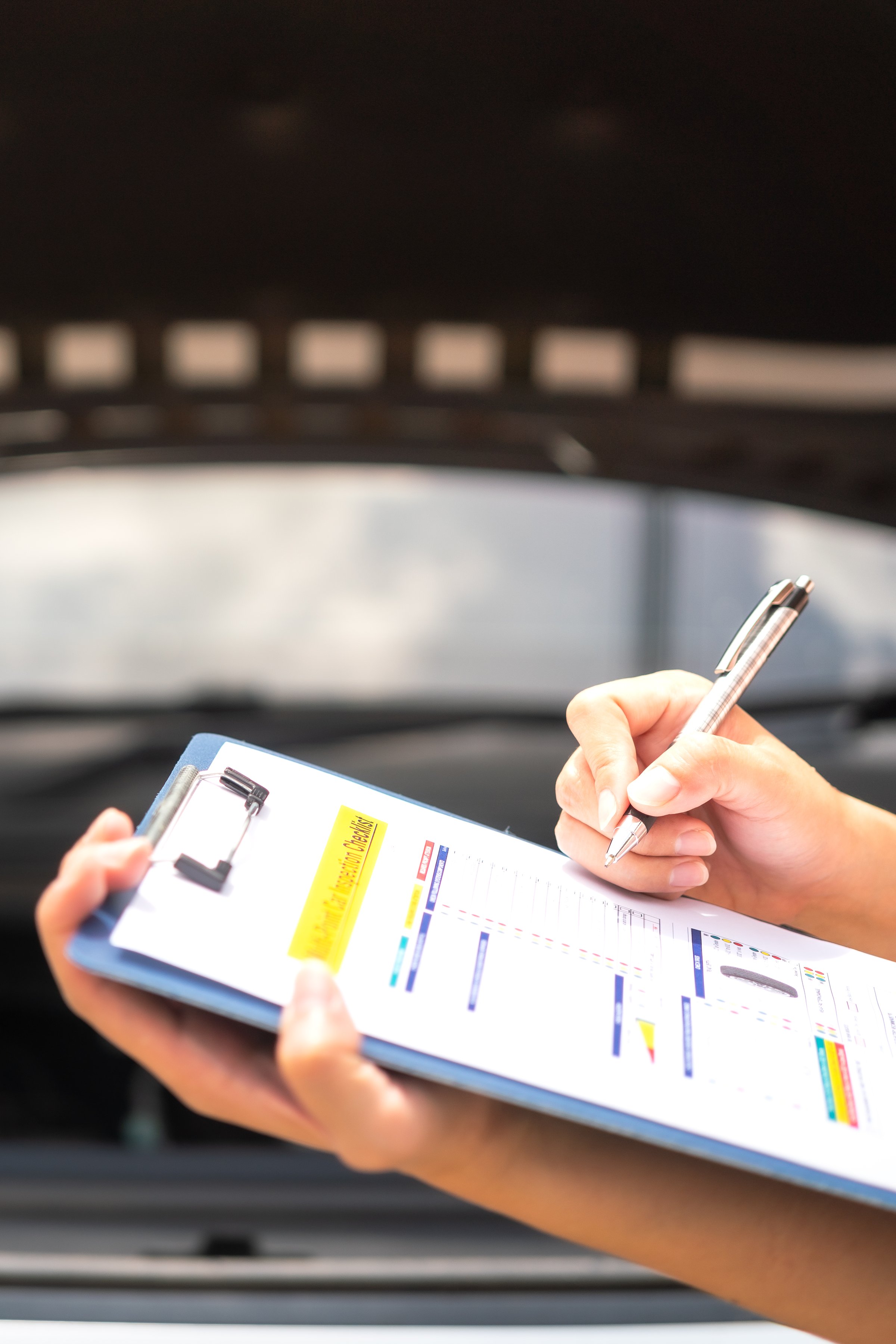 Close-up at a mechanic foreman's hand is checking on multi-point car service guideline checklist form, to verify the car service quality. Expertise working action scene, selective focus.