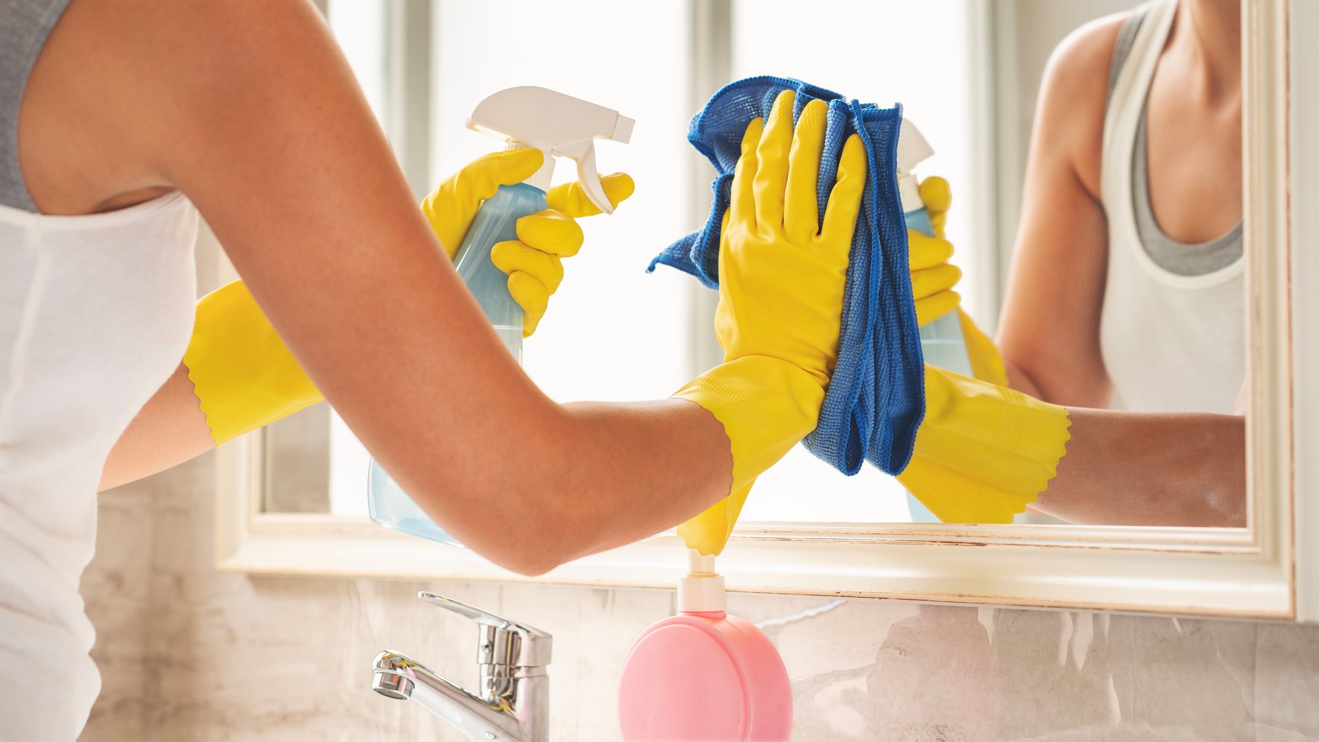 Woman cleaning mirror in bathroom