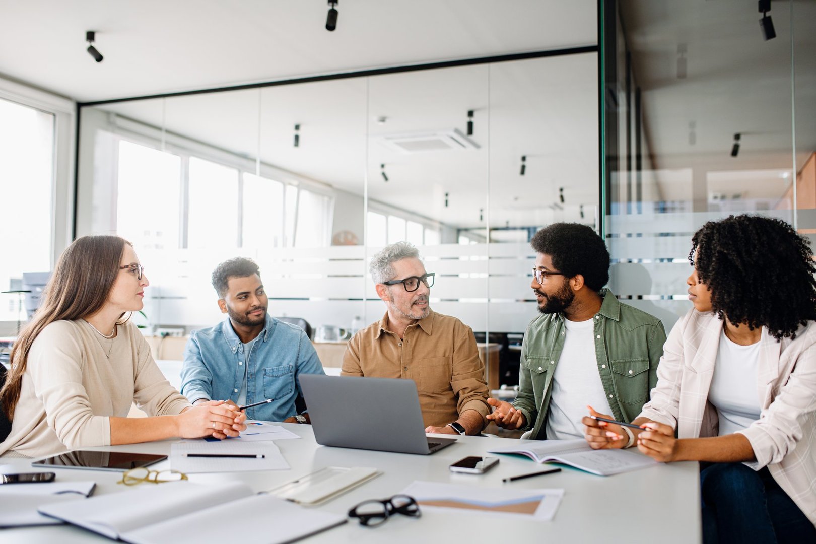 A diverse office team is engaged in a strategic meeting, with a senior colleague leading discussion, illustrating a productive and inclusive workplace. Colleagues engage in a lively exchange of ideas