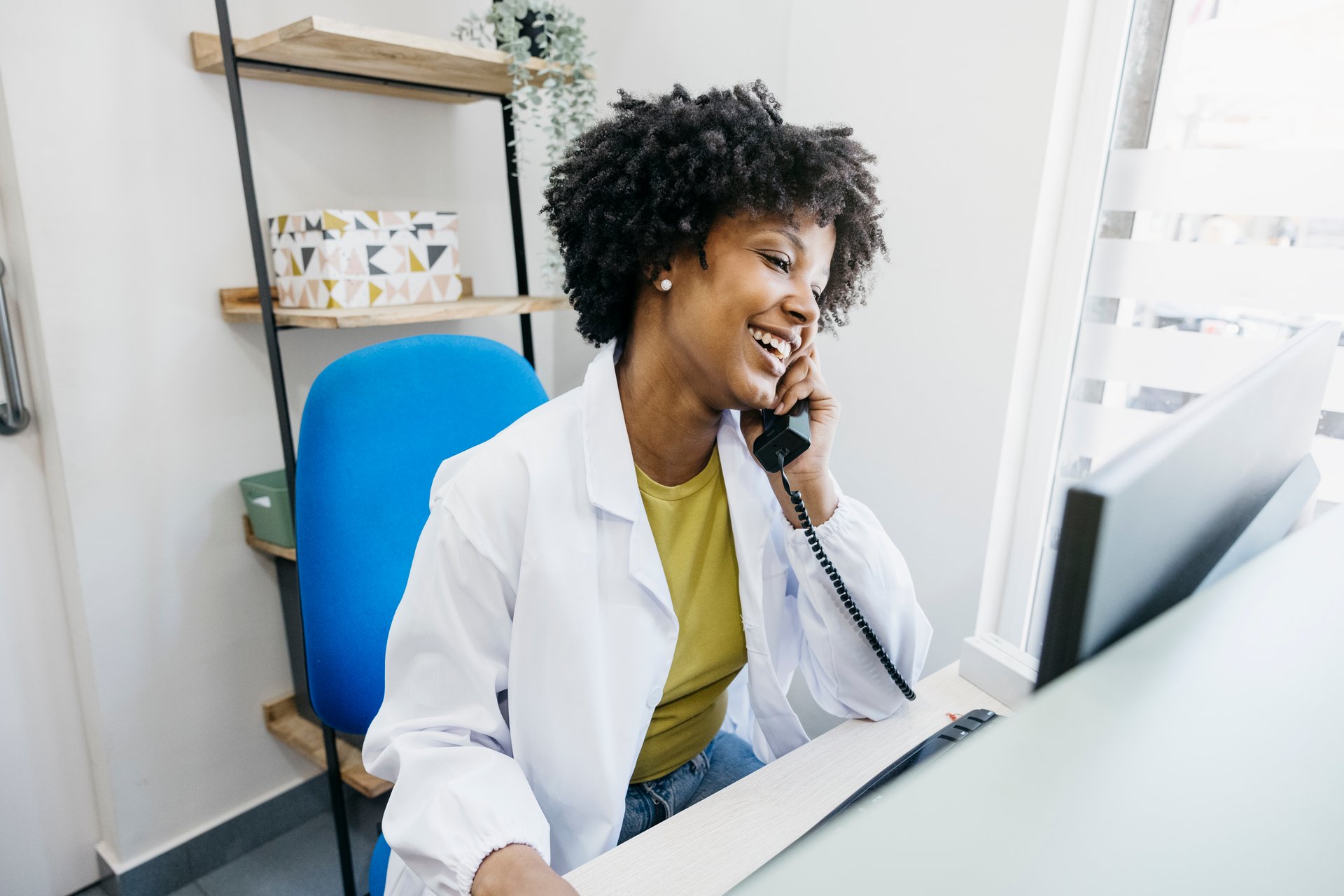 Smiling medical receptionist answering phone calls and managing appointments on her computer