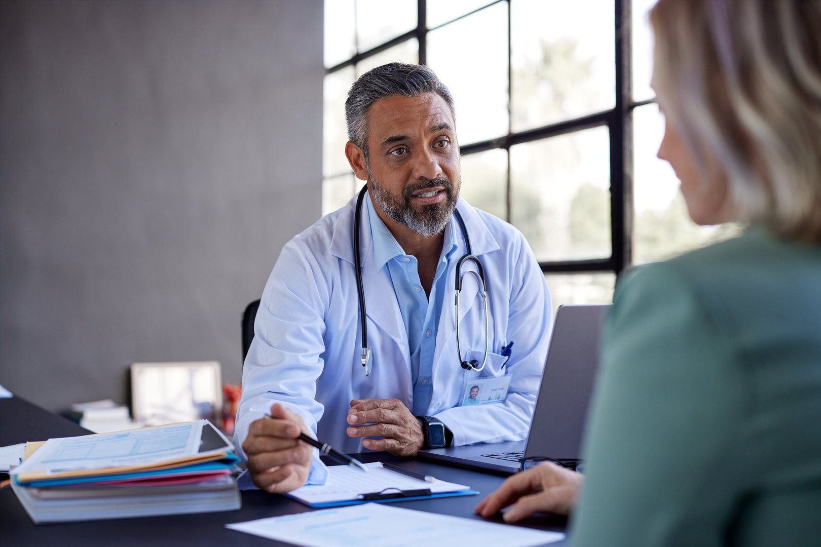 Middle eastern doctor attentively listening to a patient and providing advice. Healthcare general practitioner explaining medical options in a private appointment with his patient. Serious middle eastern physician with a female patient during a detailed consultation.