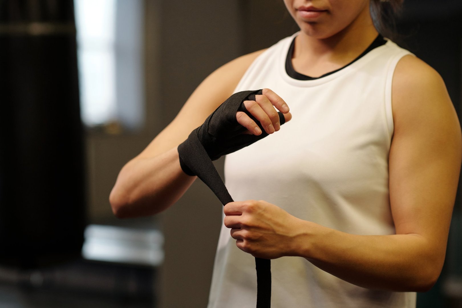 Hands of active girl wearing white activewear wrapping elastic band around wrist while standing in front of camera in gym