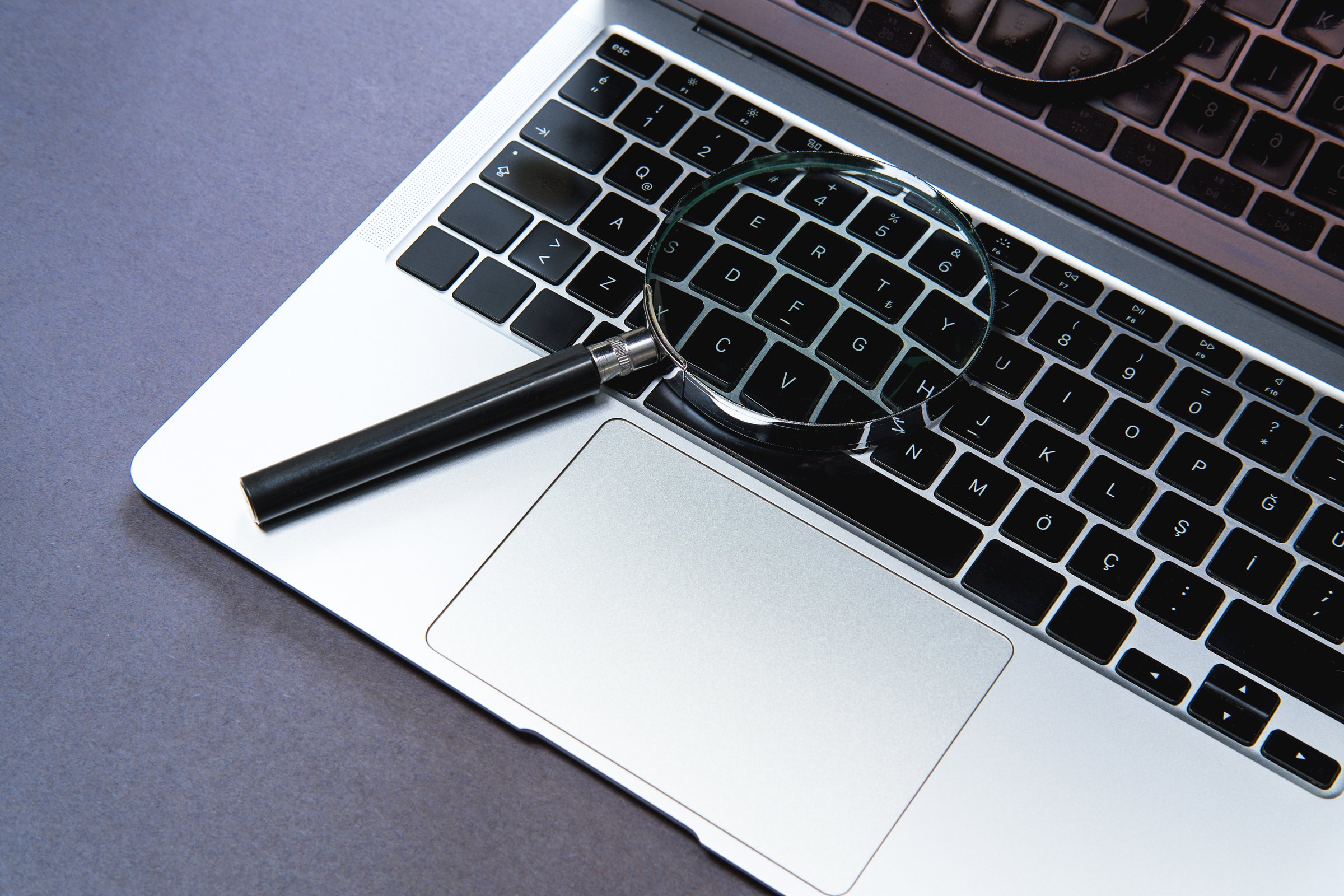 Laptop and magnifying glass on black background.
