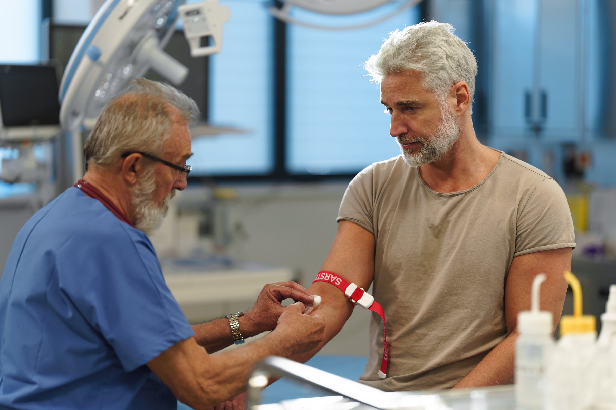 Older doctor drawing blood from patient's arm during medical examination.