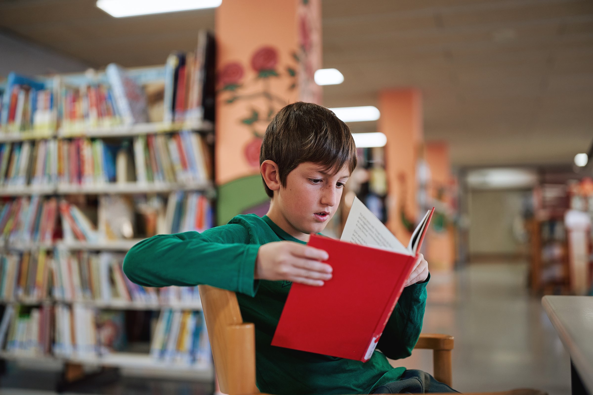Boy reading a red book in a library