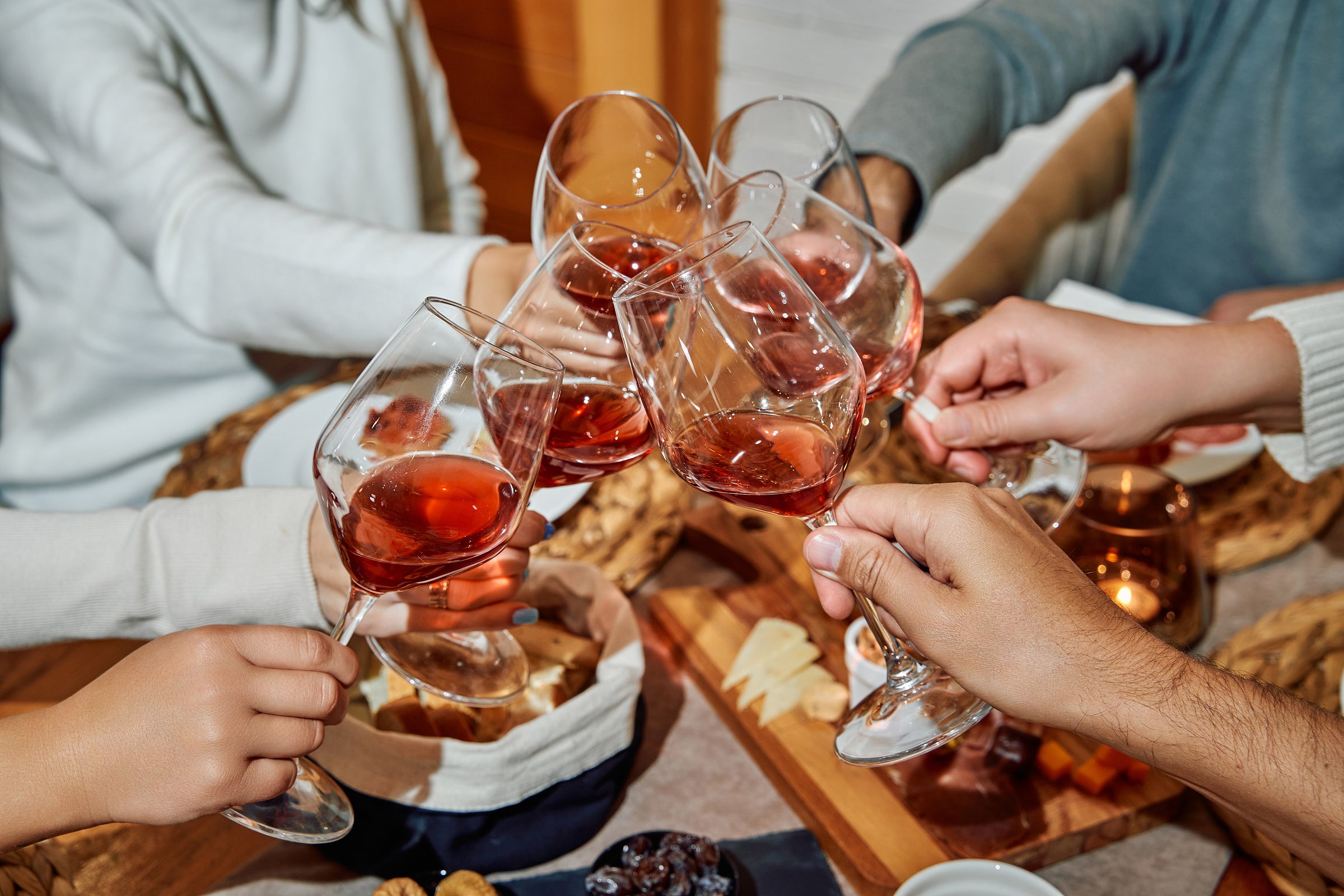 A group of friends clinks glasses filled with red wine, celebrating togetherness at a cozy, indoor gathering, emphasizing friendship and joyful moments.