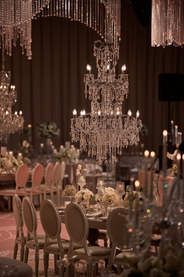An exquisite close-up of a luxurious wedding table setup featuring a stunning crystal chandelier, elegant floral arrangements, and candlelit decorations. Perfect for showcasing wedding inspiration, event design, or luxury dining themes.