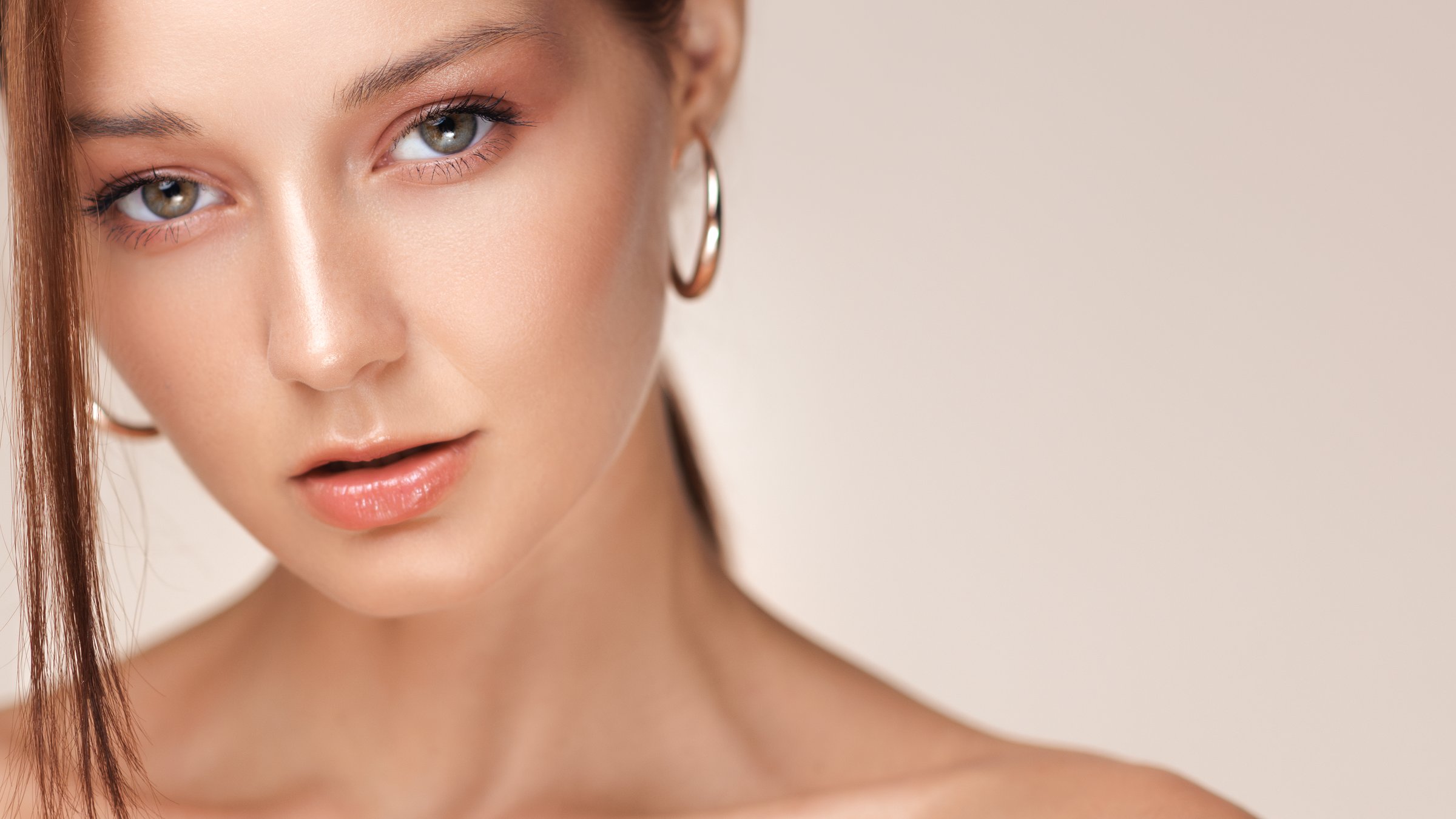 High quality beauty close-up of a young Caucasian woman with natural glowing makeup, glossy lips, and hoop earrings. Perfect for cosmetics, skincare, jewelry, and luxury lifestyle promos.