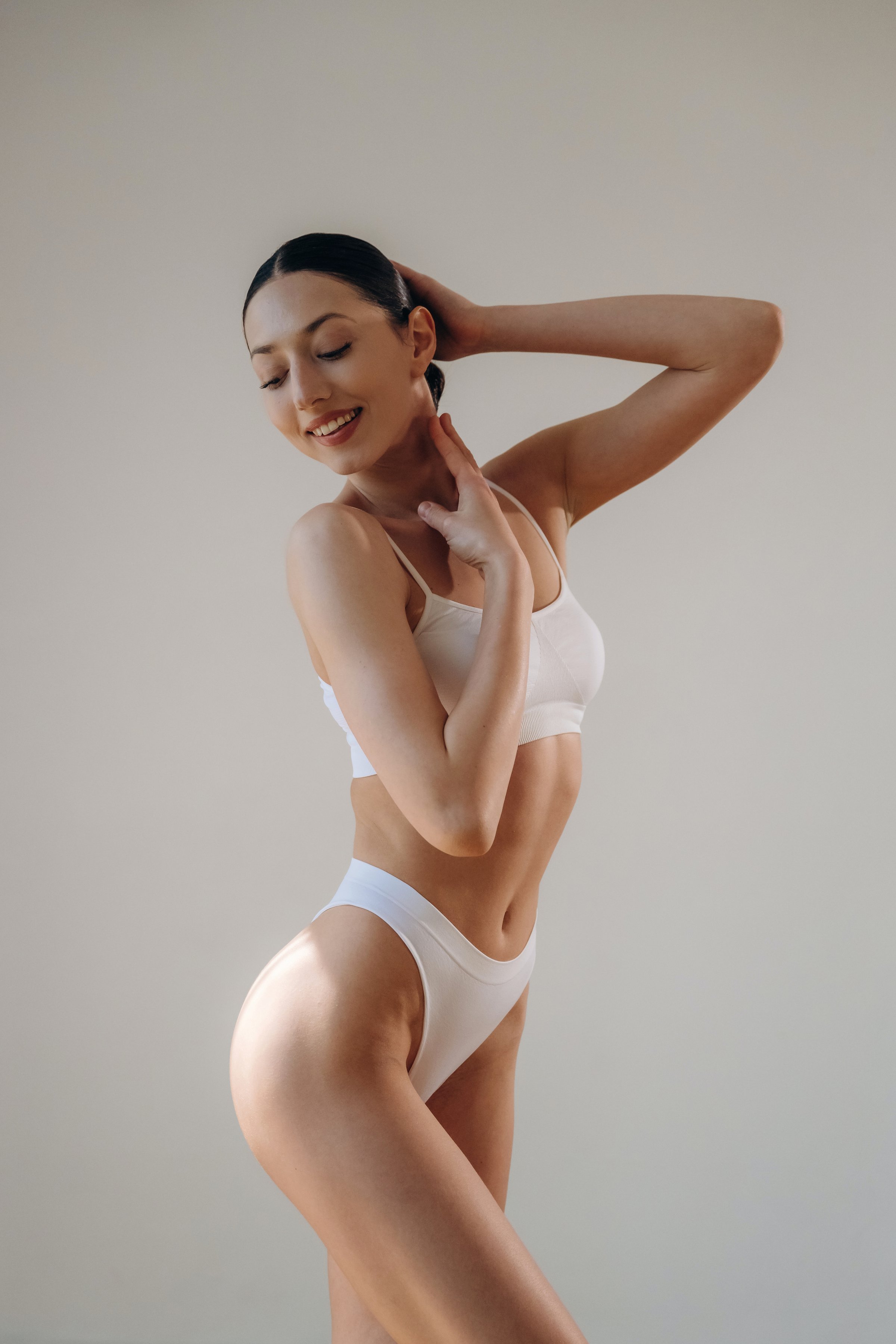 White creamy background. Young woman in sportive clothes is against the wall.