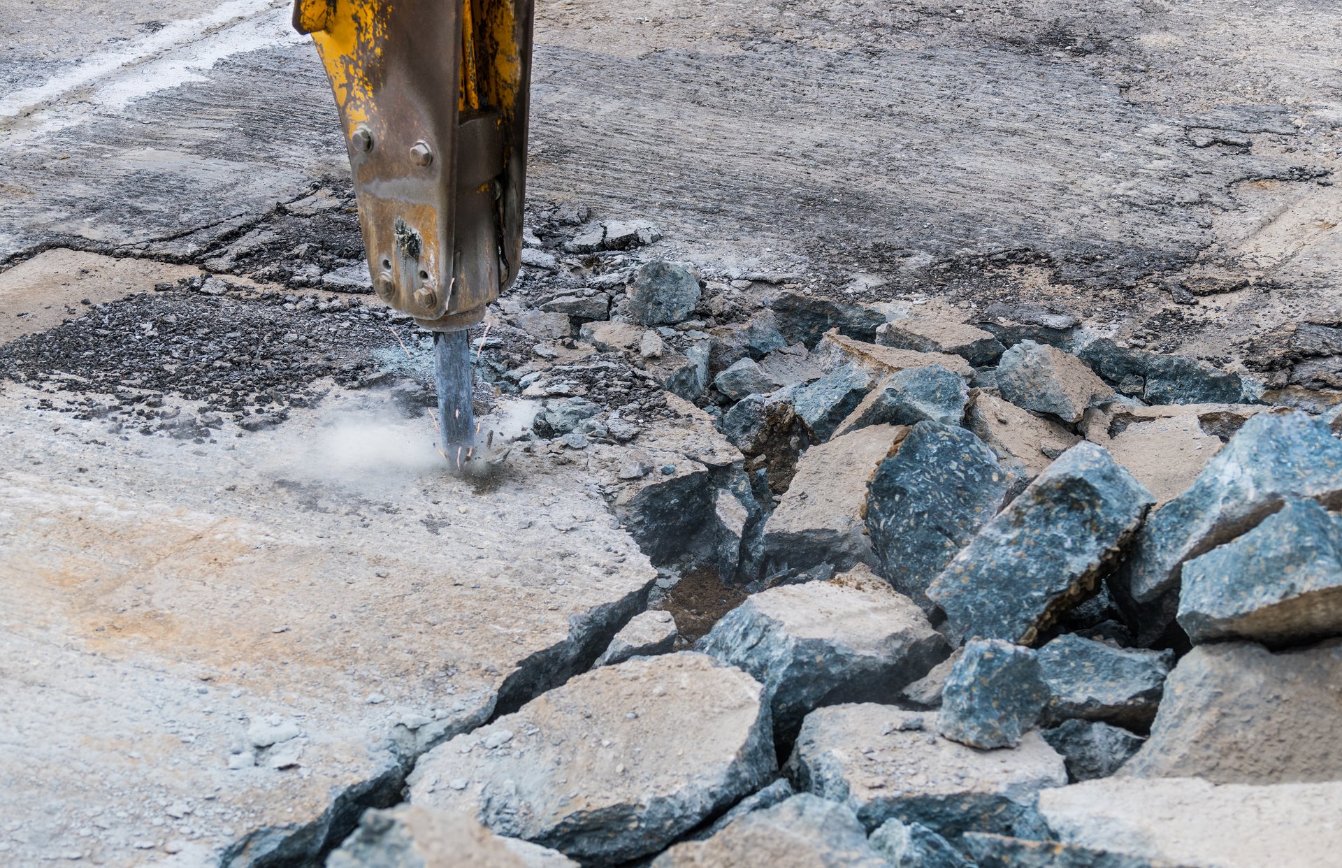 Detail of hydraulic jackhammer mounted on excavator arm working at old road reconstruction. Repairs in civil engineering