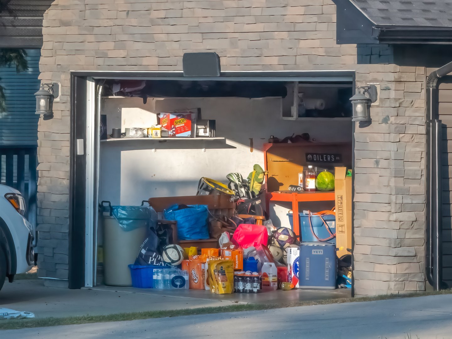 Calgary, Alberta, Canada. Jun 8, 2025. A sunlit garage stands open, revealing a clutter of household items, storage bins, hinting at a need for organization.