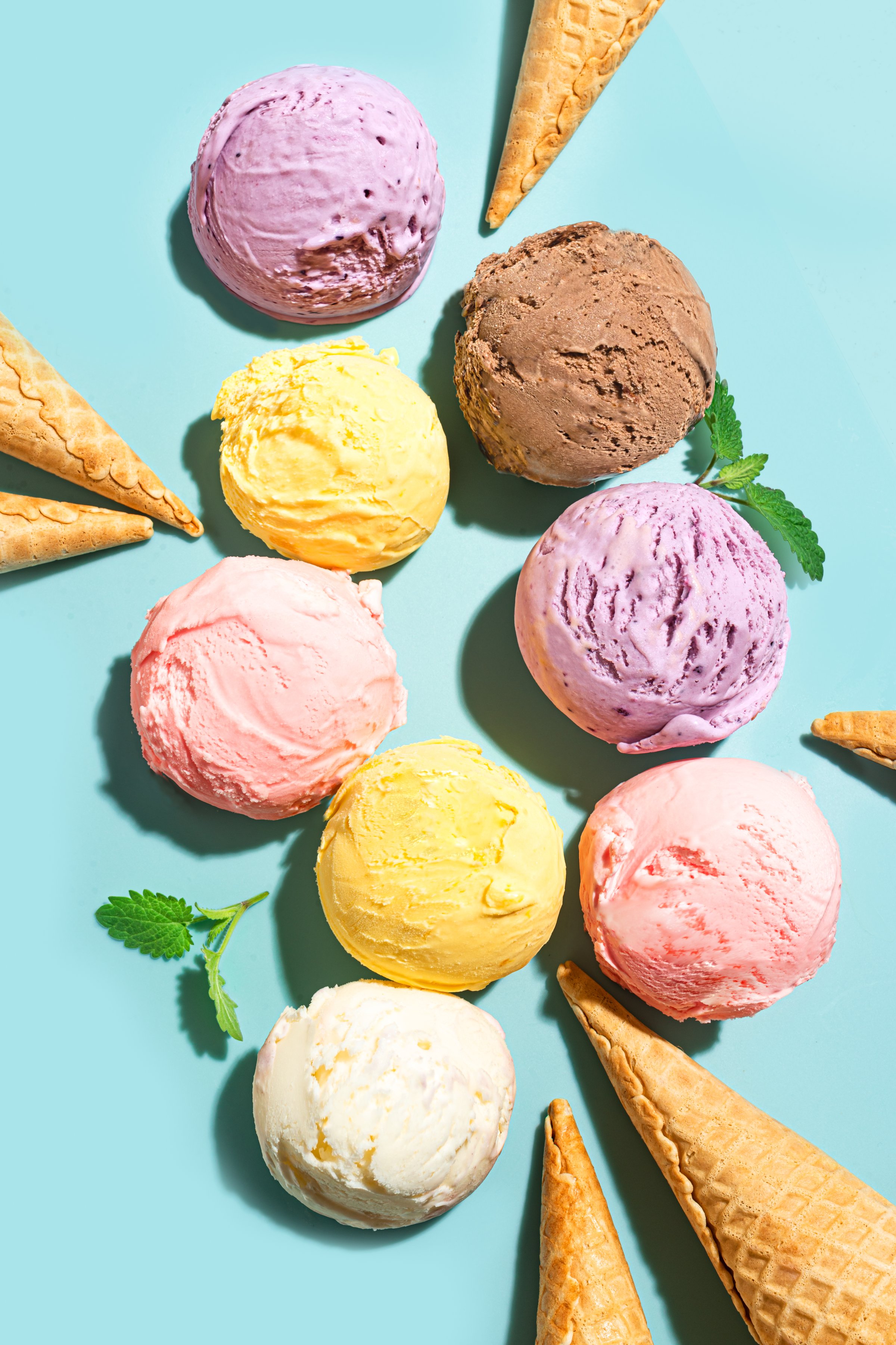 Assorted scoops of ice cream and waffle cones creative layout on blue background, top view. Various ice creams or gelato trendy design.