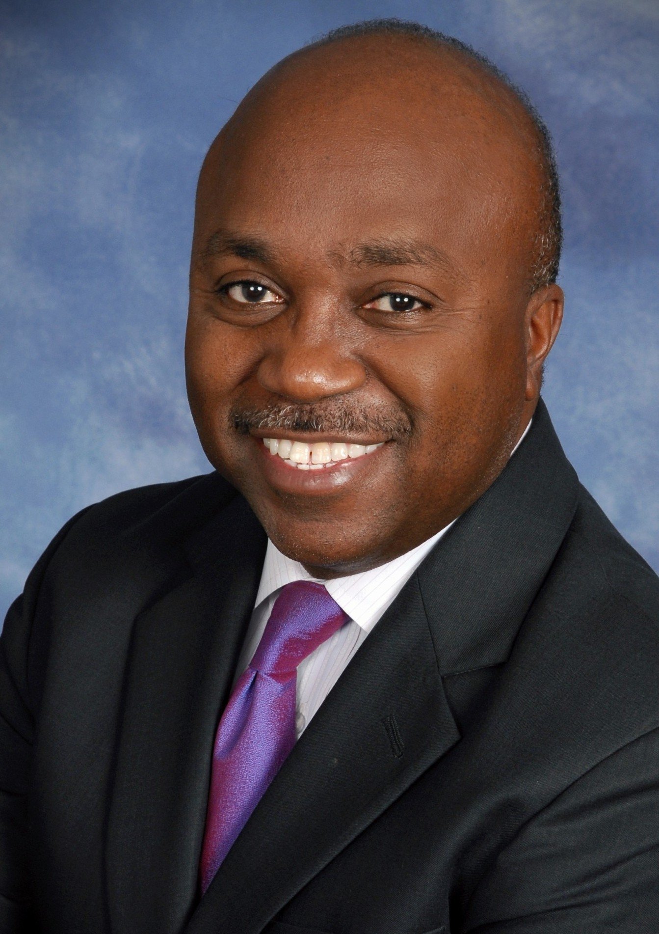 Smiling man in a suit and tie against a blue background.