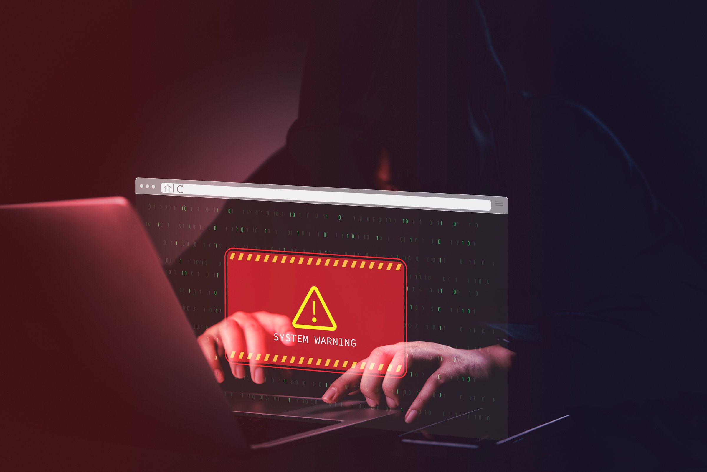 hacker in a dark room with a laptop red System Warning on the screen. Concept of cyber threats and cybersecurity breach alert with binary code online internet technology.