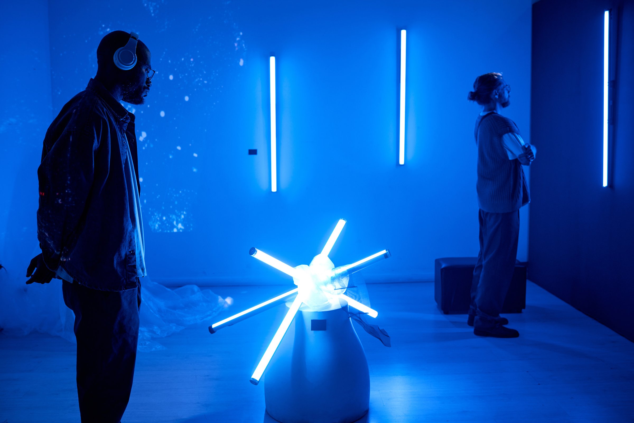 Individuals enjoying a futuristic art installation in a dark room illuminated by neon lights Both people are wearing headphones, enhancing their immersive experience