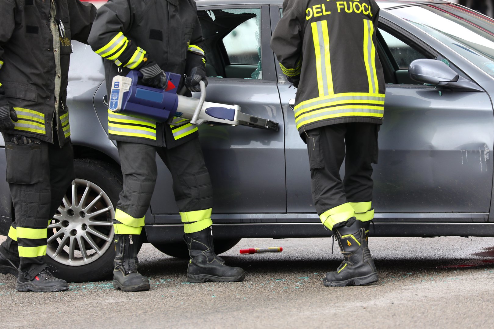 Vicenza, VI, Italy - team of firefighters wearing uniforms tear off a car door with hydraulic shears after the road accident to save the injured person
