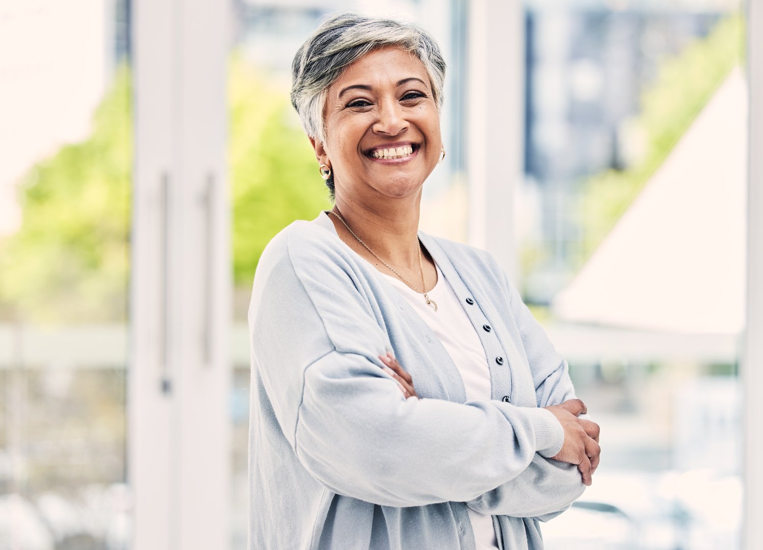 Portrait, happy and senior woman with arms crossed in house for positive mindset, relax in retirement home and joy. Face, smile and elderly female person from India with confidence in casual clothes.