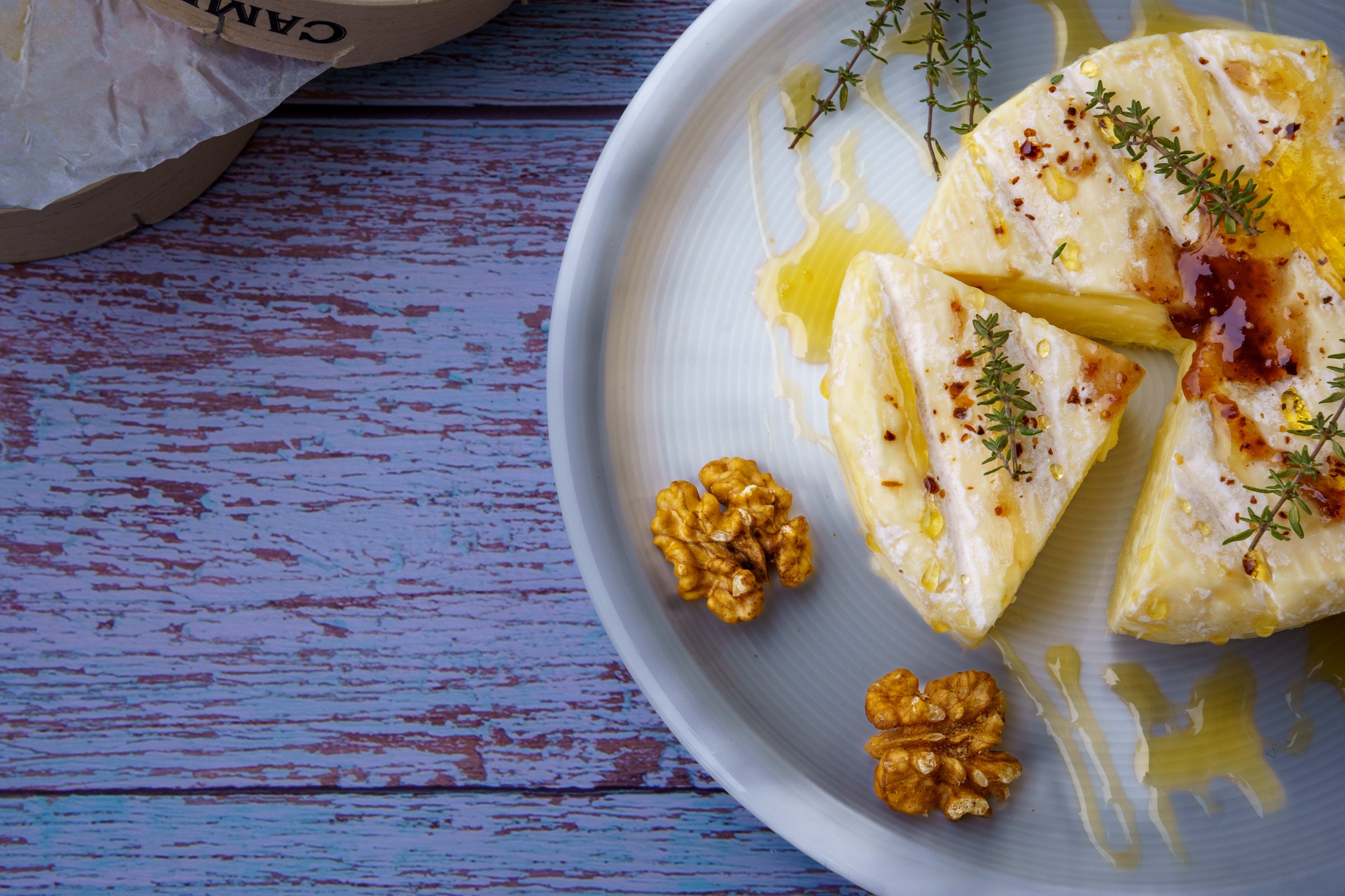 Baked Camembert, traditional creamy gourmet round cheese from France with honey, fig jam, thyme and walnuts. White plate on rustic wooden background. Close up, top view