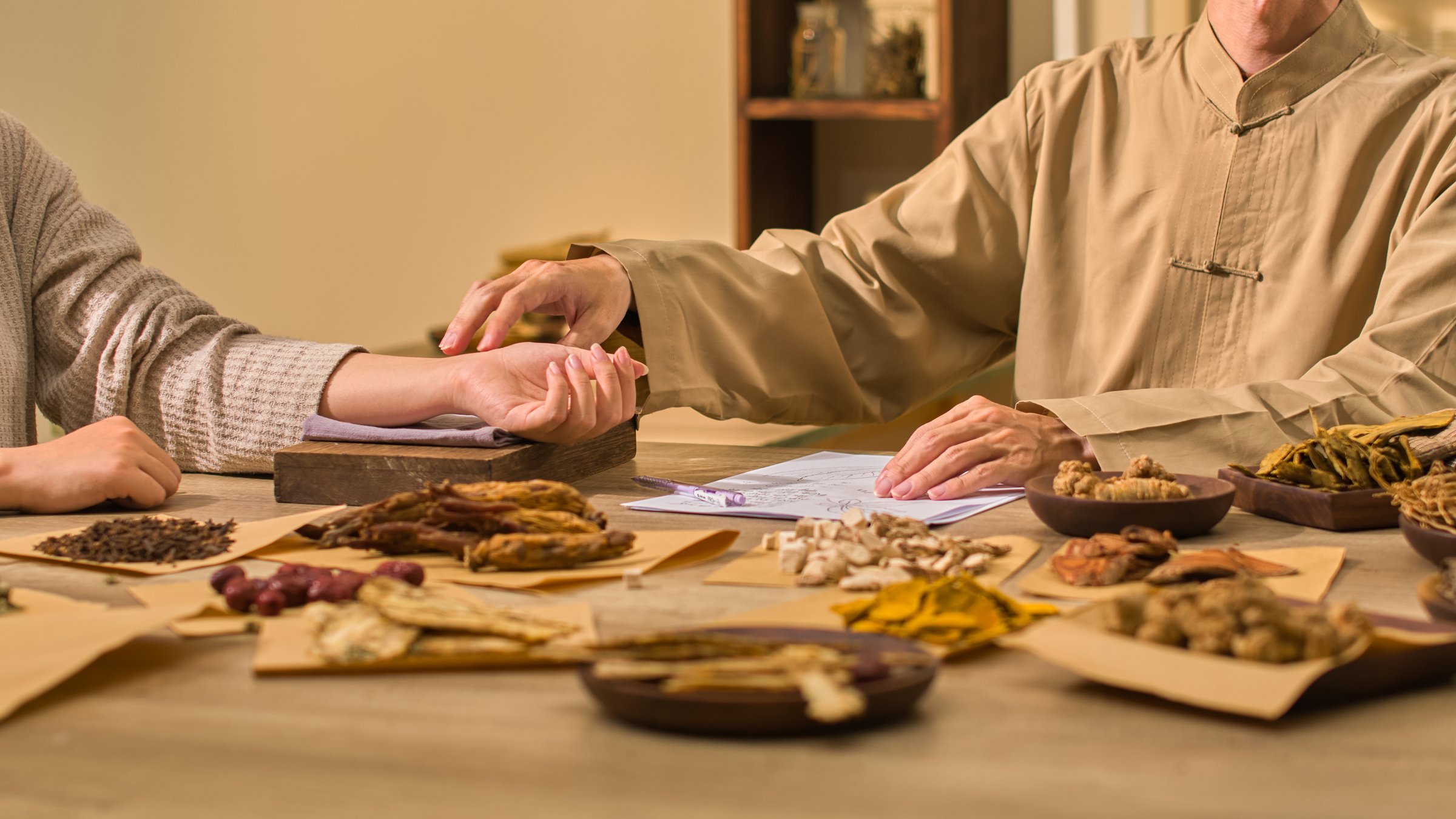 The method of taking a patient's pulse involves extending and placing their hand on a wooden board wrapped in cloth. The template photo shows a traditional medicine clinic with many plants on display.