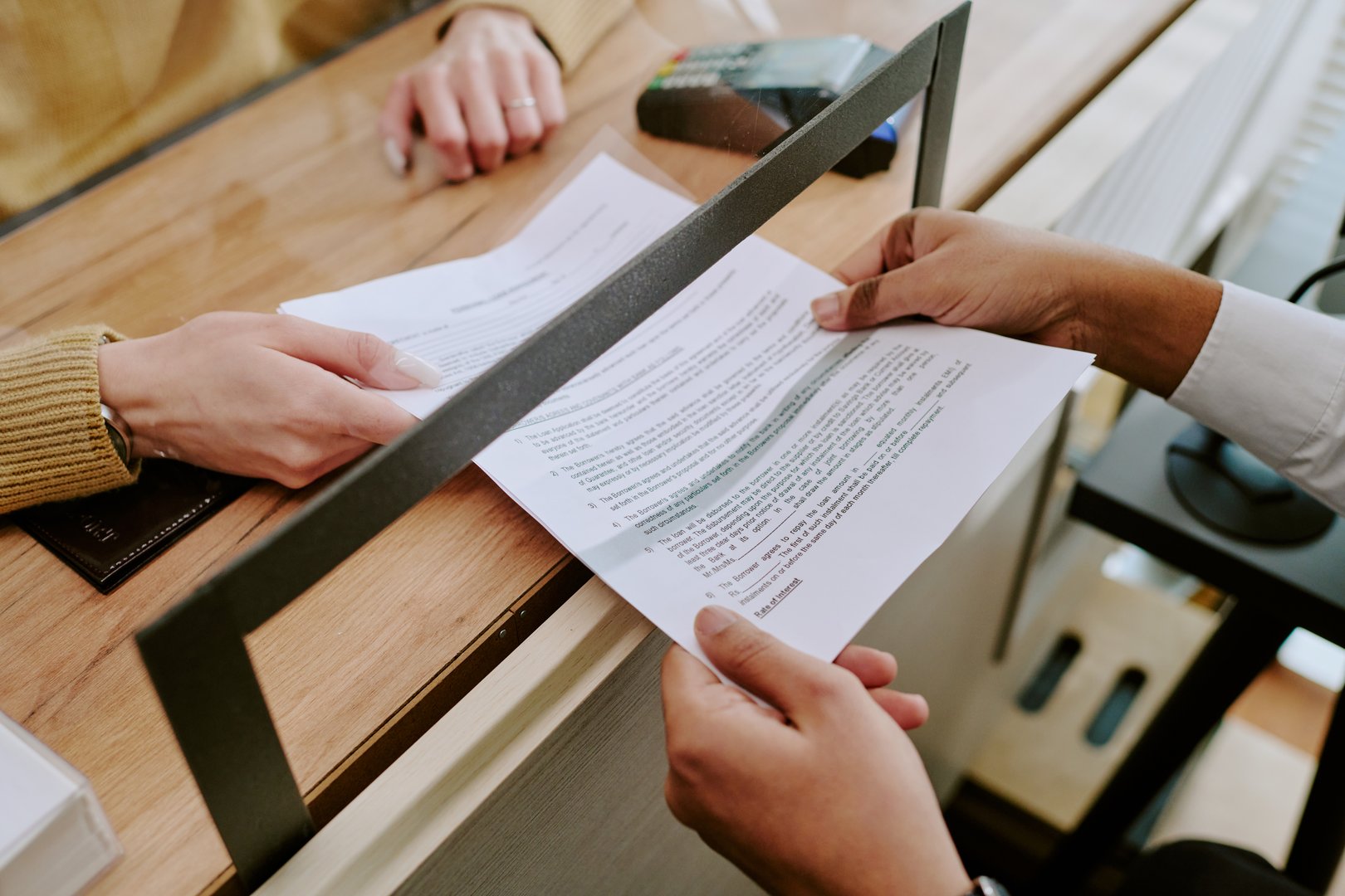 Hands of two people signing an official document at an office counter, with a payment terminal and other materials in background, collaborative atmosphere for business dealings