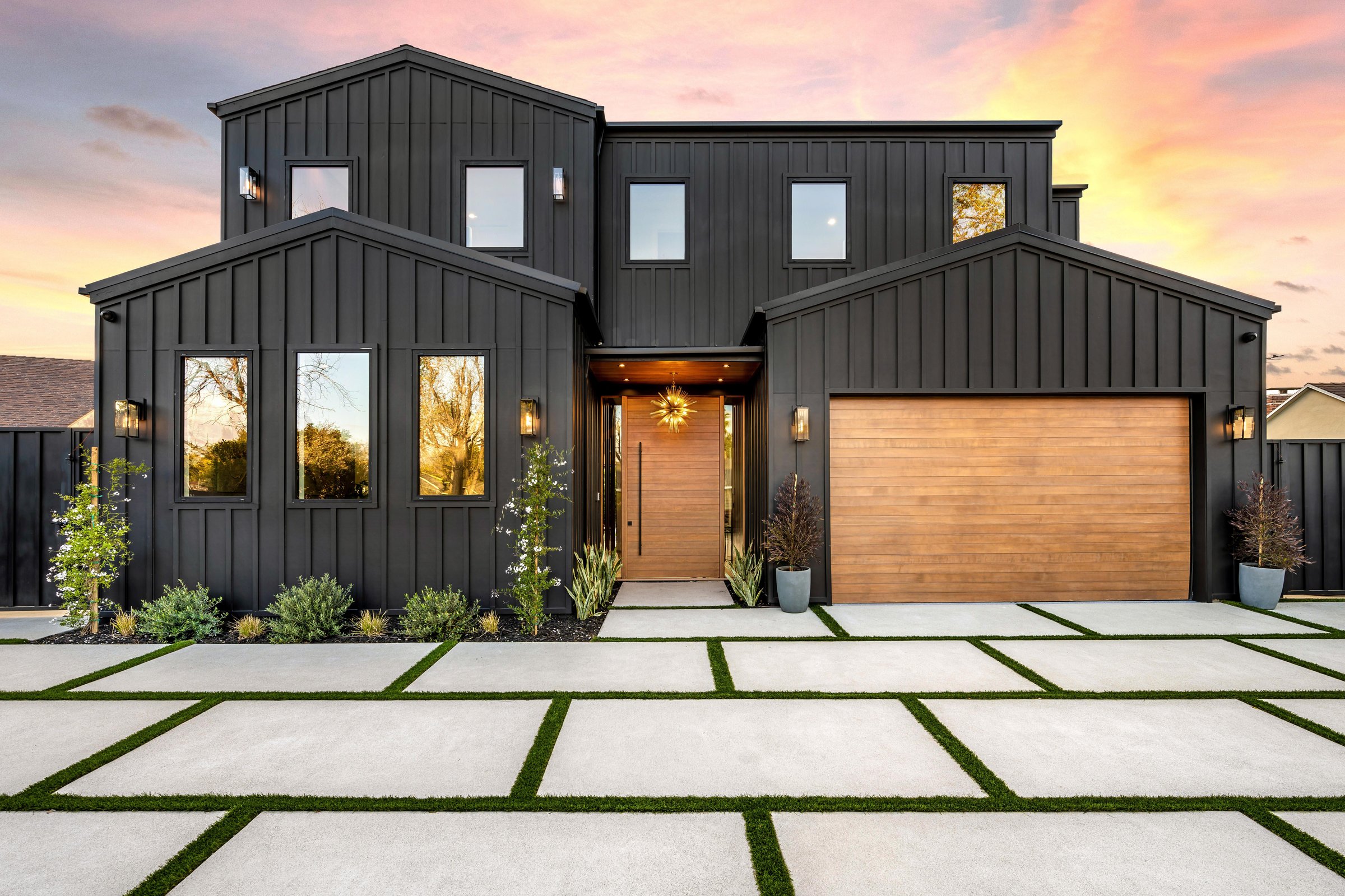 Modern black house exterior with wooden garage door and driveway at sunset.