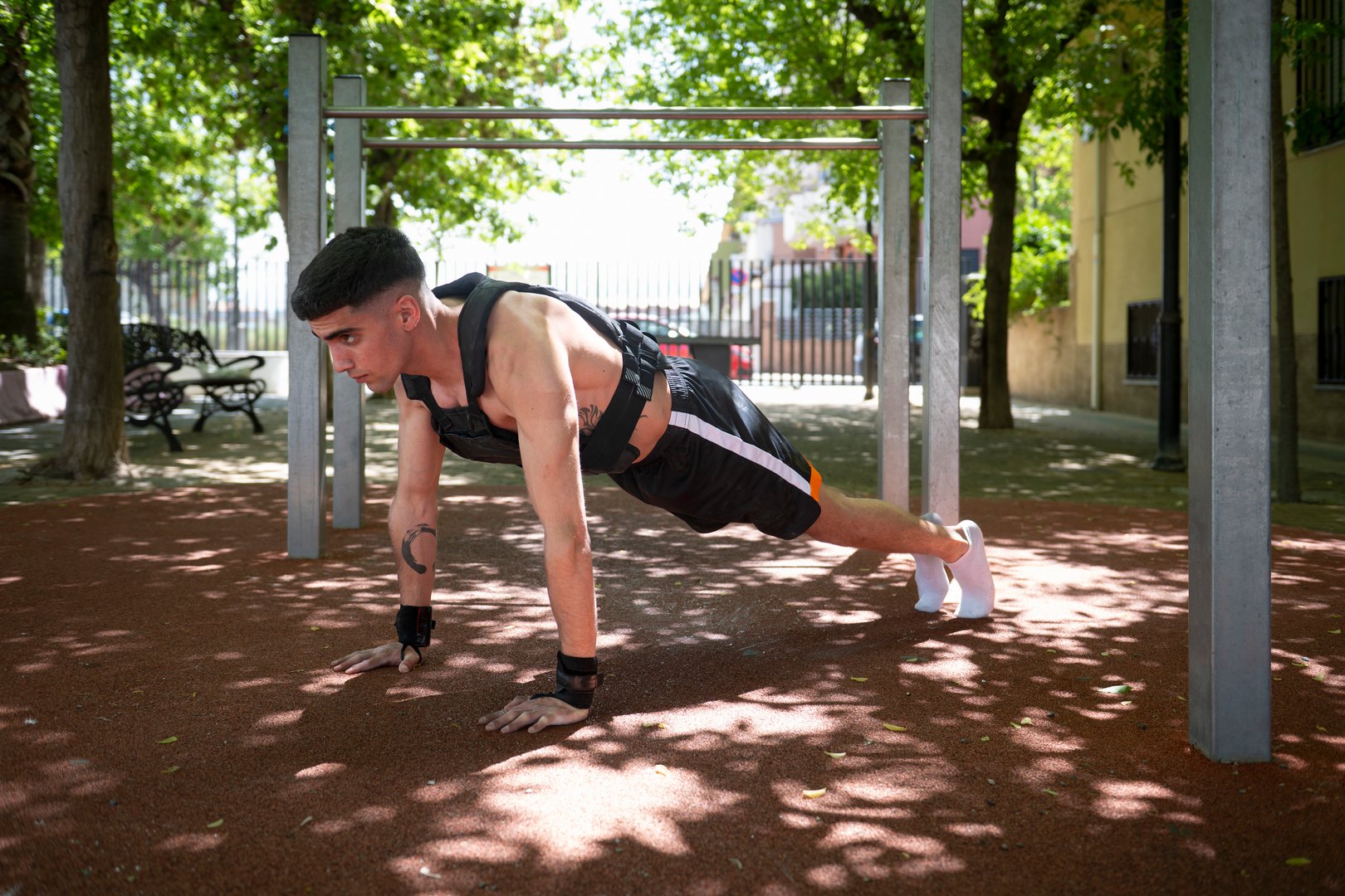 Determined male athlete performing plank exercise, part of calisthenics workout, wearing weighted vest in outdoor park setting, demonstrating strength and fitness