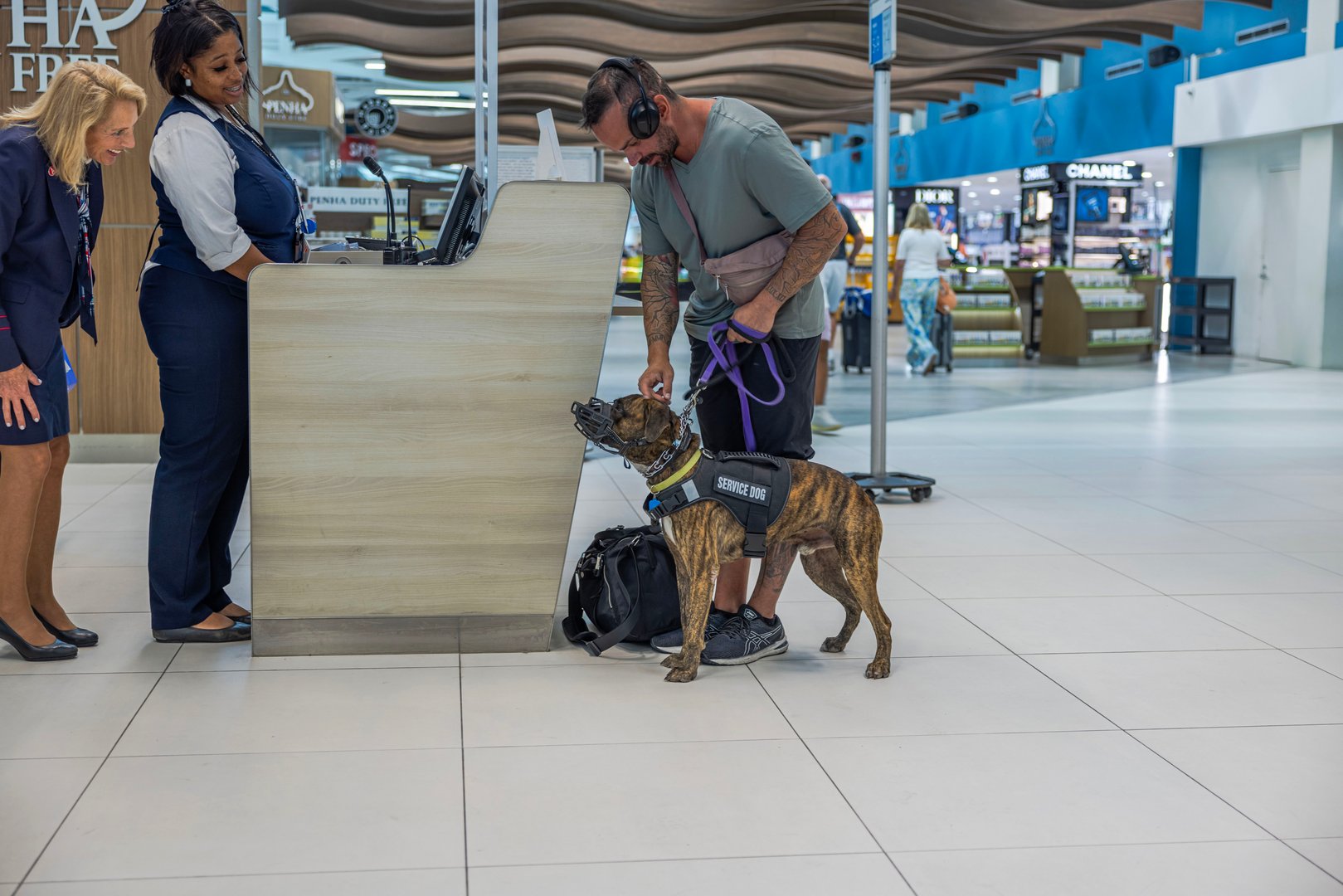 Willemstad. Curacao. 01.16.2025. Man with service dog interacting with airport staff at check-in counter inside modern terminal.