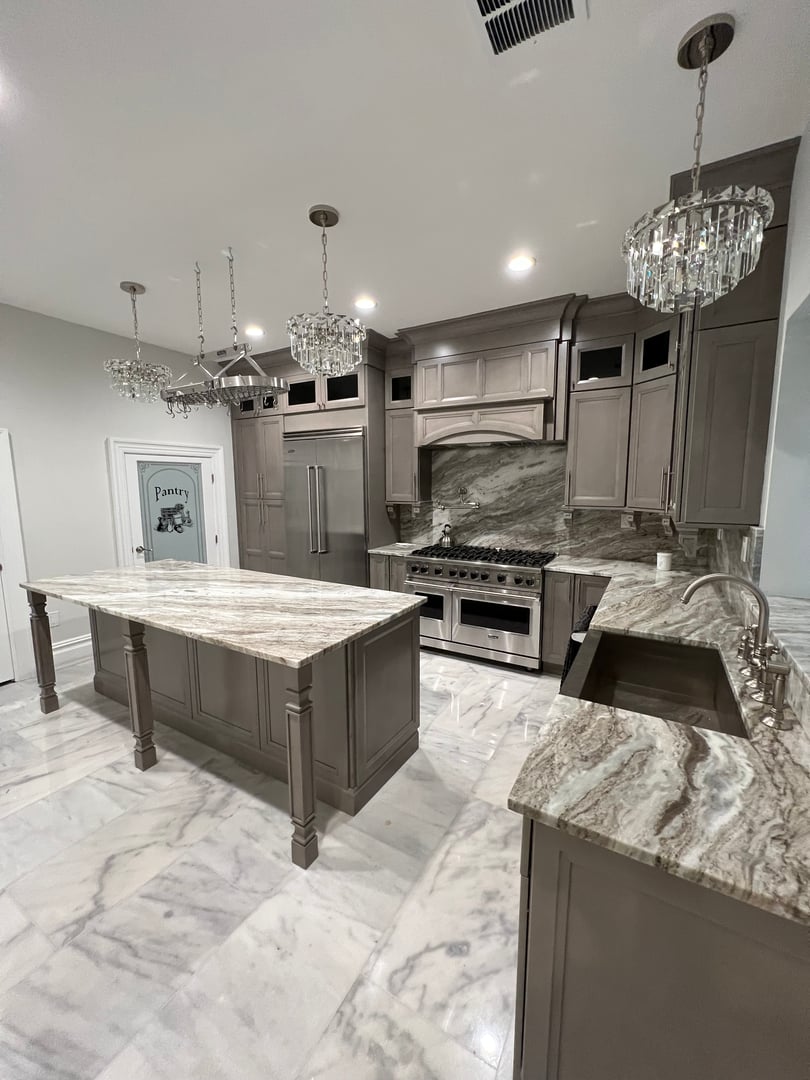 Modern kitchen with marble countertops, island, stainless steel appliances, and chandelier lighting.