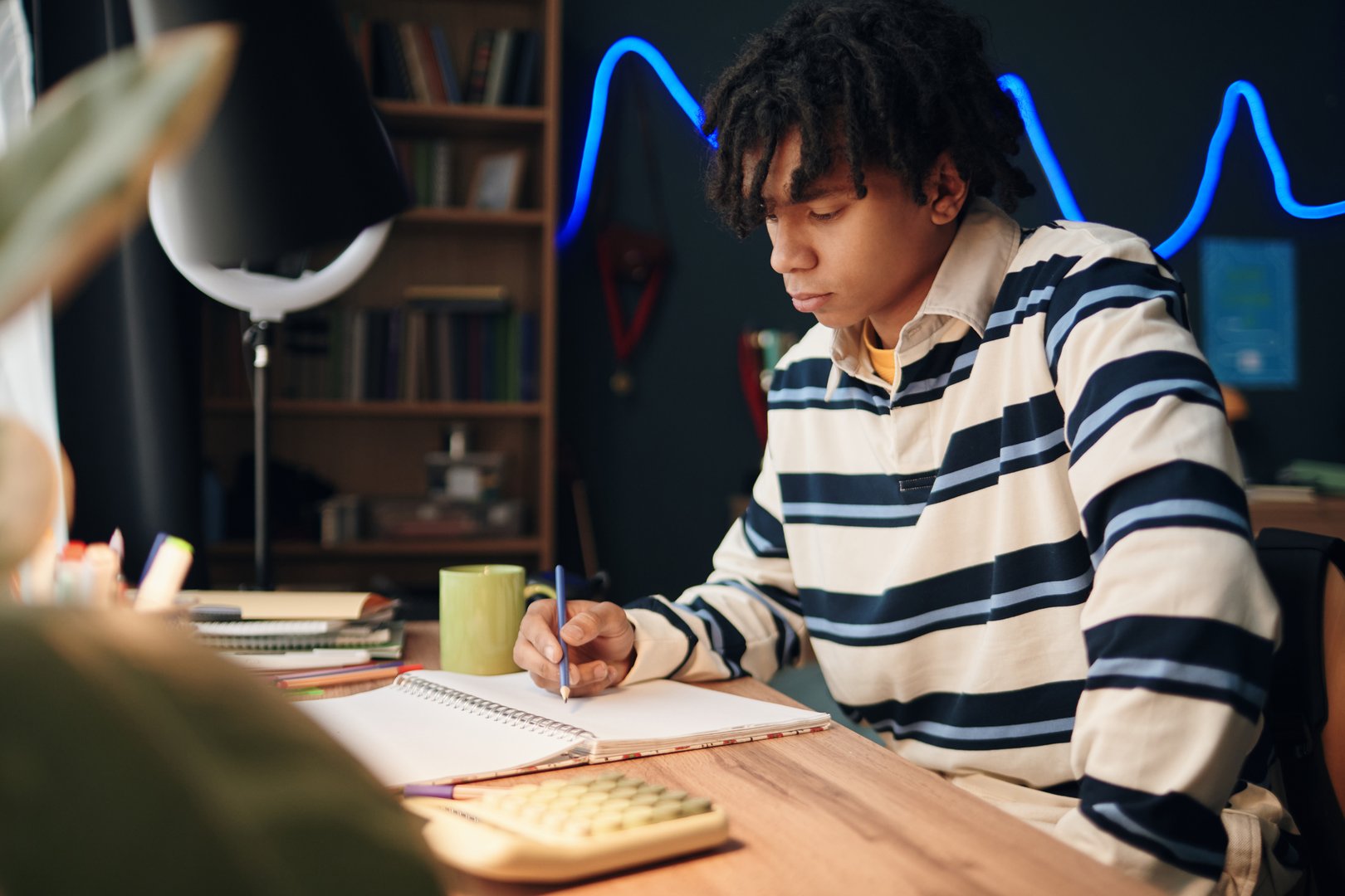 Teenage boy studying at desk with notebook and calculator
