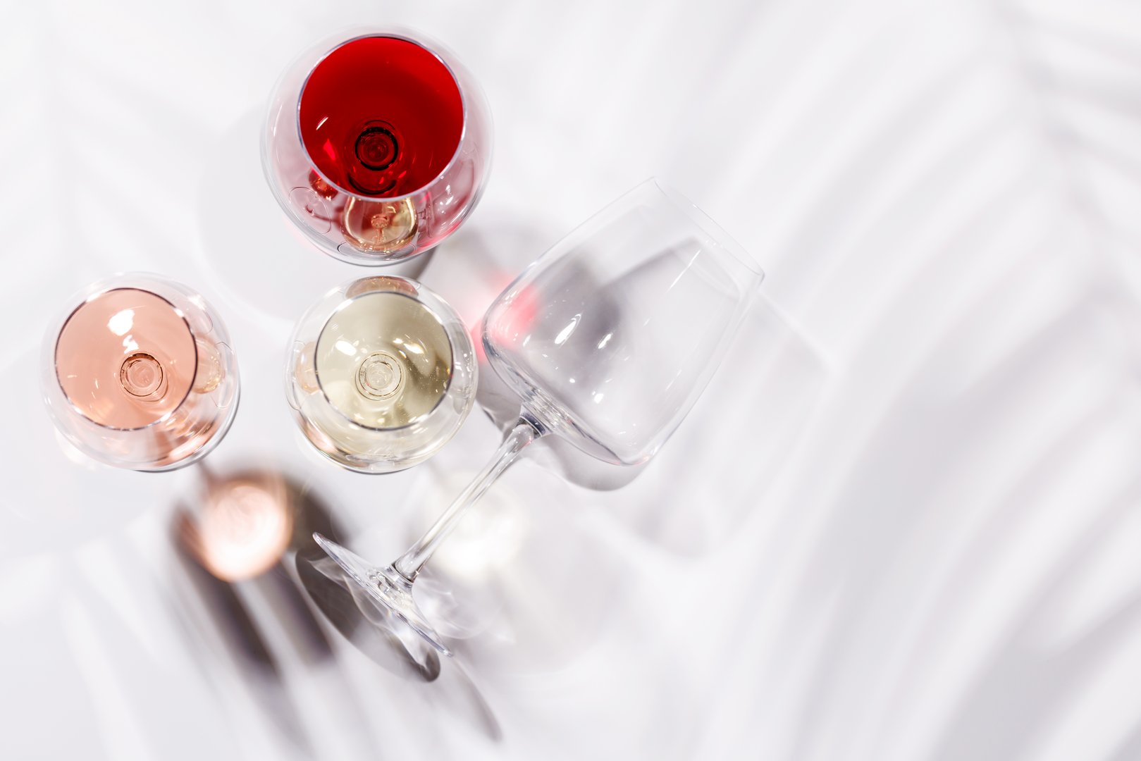 Three wine glasses filled with red, white, and rose wine, standing gracefully on a bright, minimalist background. A vibrant display of wine's variety and elegance