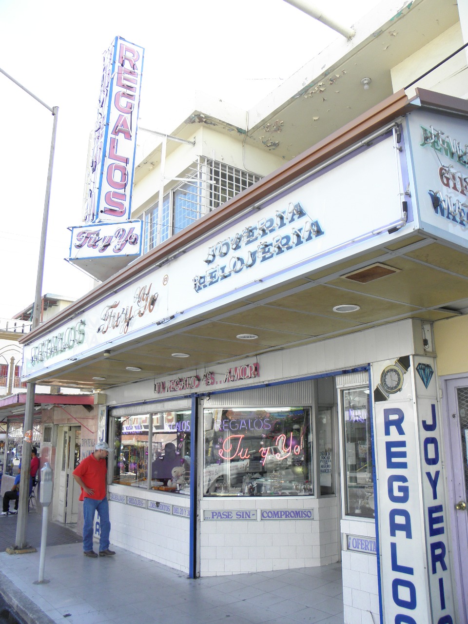 Storefront of "Regalos Tu y Yo," a gift and jewelry shop with signs in Spanish, located on a city street corner.