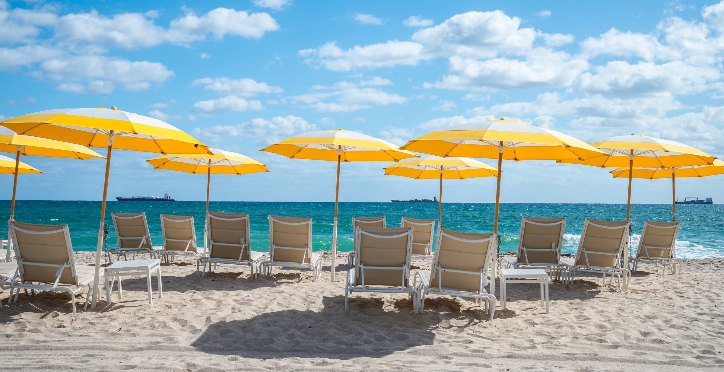 Row of luxury beach chairs and yellow umbrellas on white sand. Sea view in Fort Lauderdale, Florida. No people. Summer vacation.
