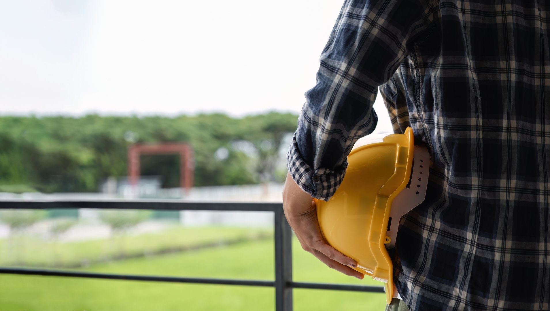 Male engineer standing holding safety helmet looking out at construction site..