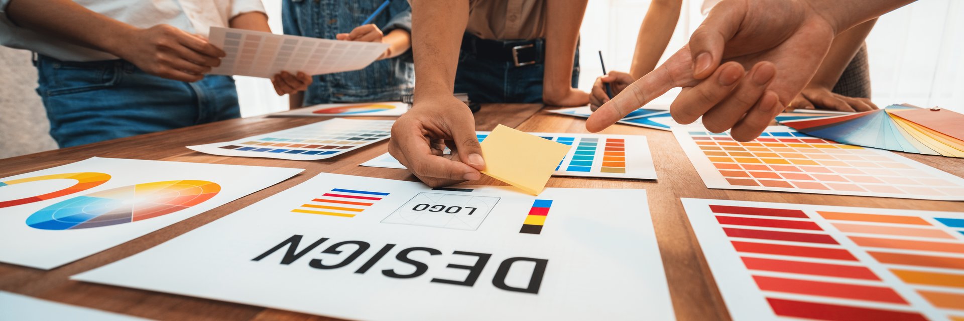 Graphic designer brainstorm logo and graphic art at busy creative studio workshop. Experiment and brainstorm color palette and pattern at workspace table for creative design. Panorama shot. Scrutinize