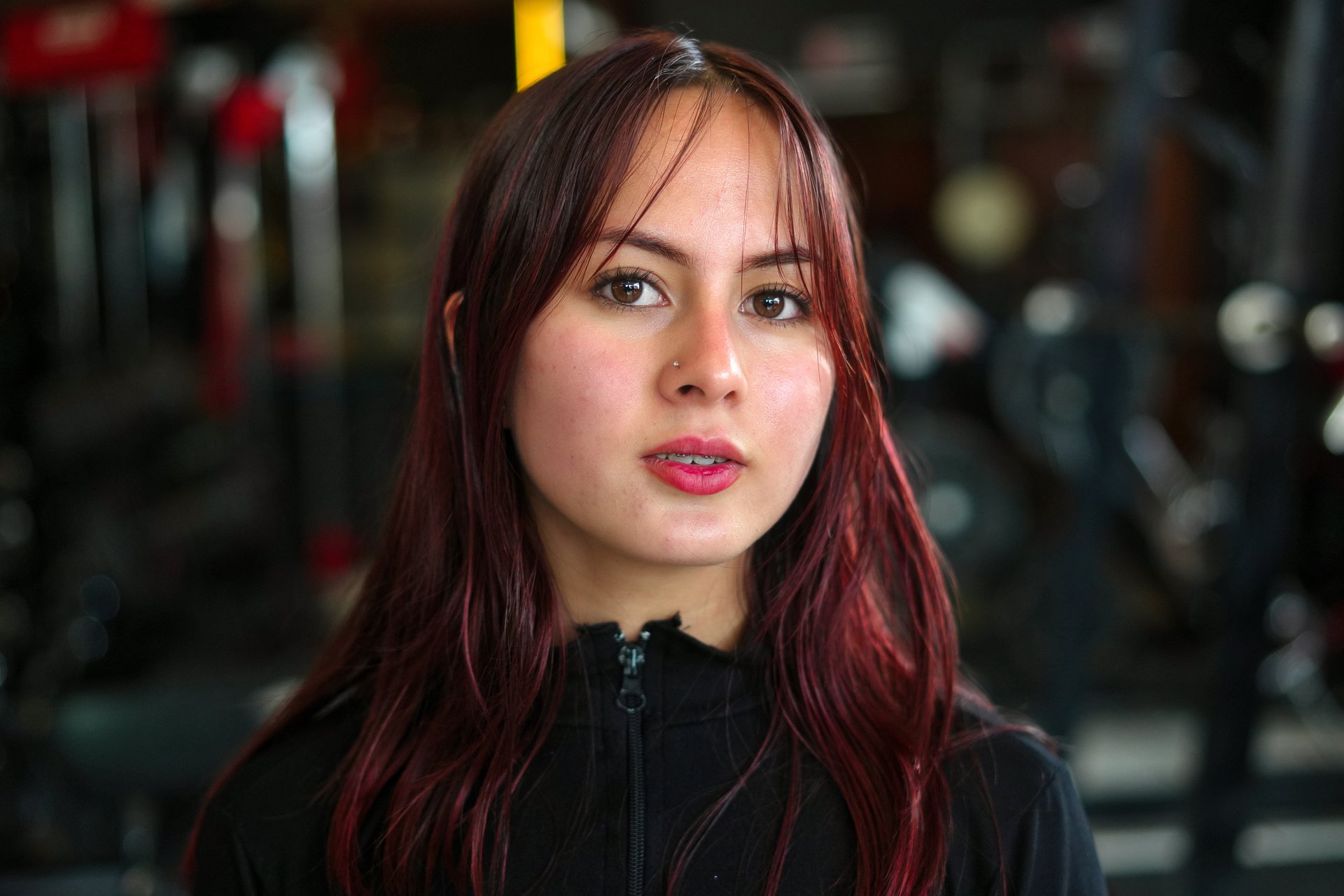 Young red-haired woman in activewear with a serious, focused expression posing in a gym upper-body portrait conveying strength, determination and healthy lifestyle