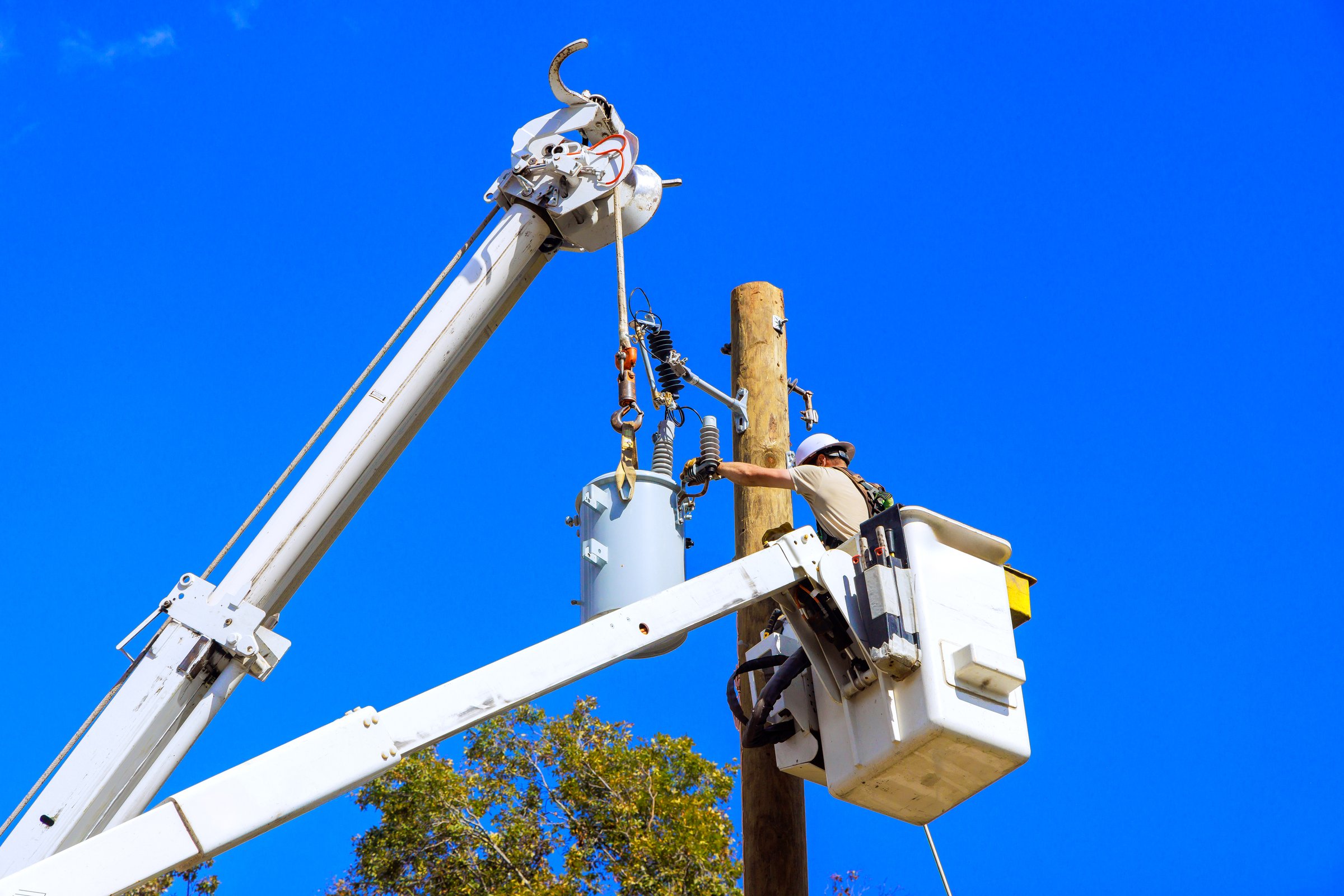 Worker in bucket lift fixes electrical components on utility pole during work day