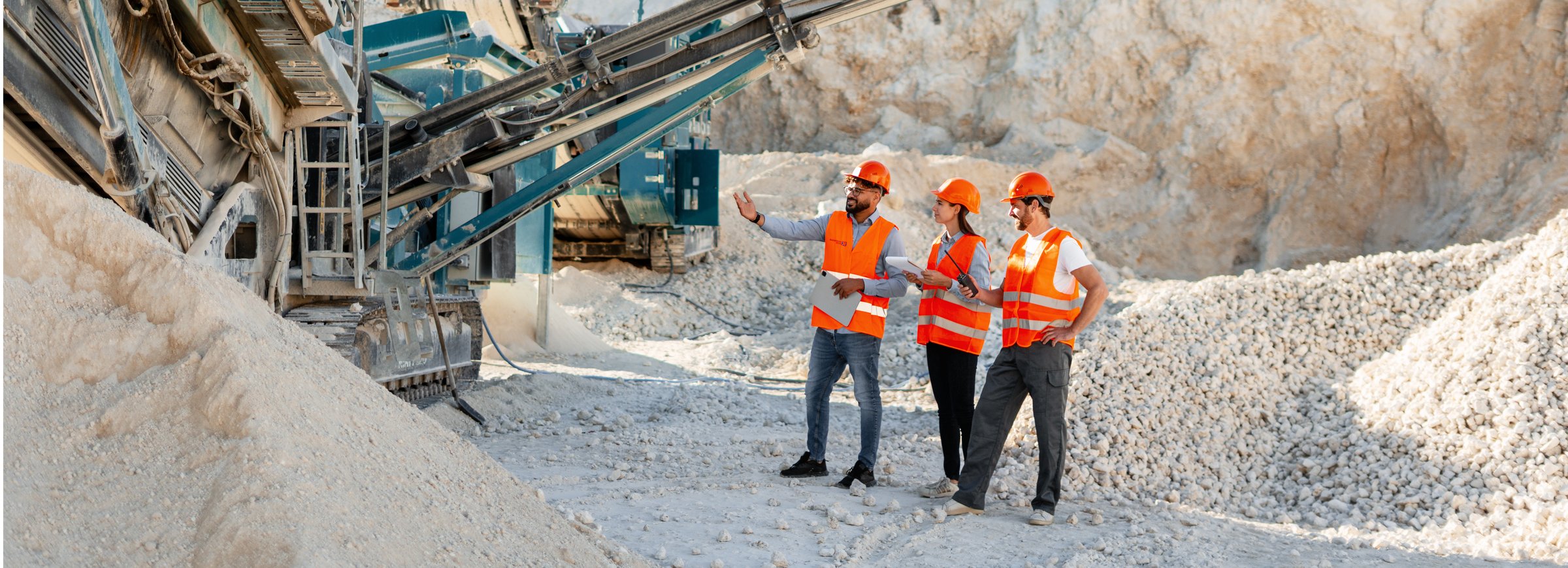 Engineers wearing safety vests and helmets inspecting a rock crushing machine in a quarry