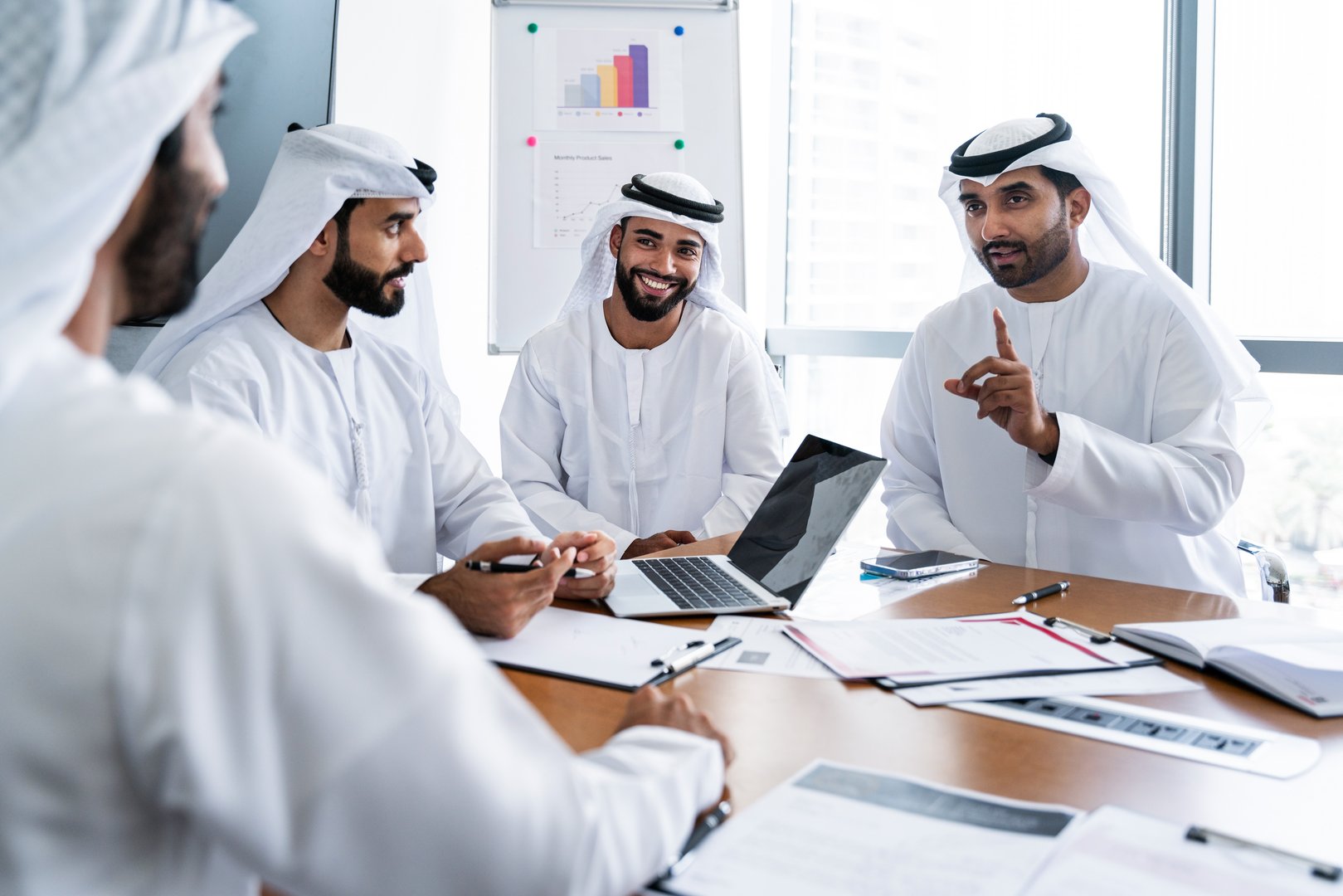 Arab businessmen wearing emirati kandura meeting in office for business deal - Corporate business group of middle-eastern people working in an international company in middle east