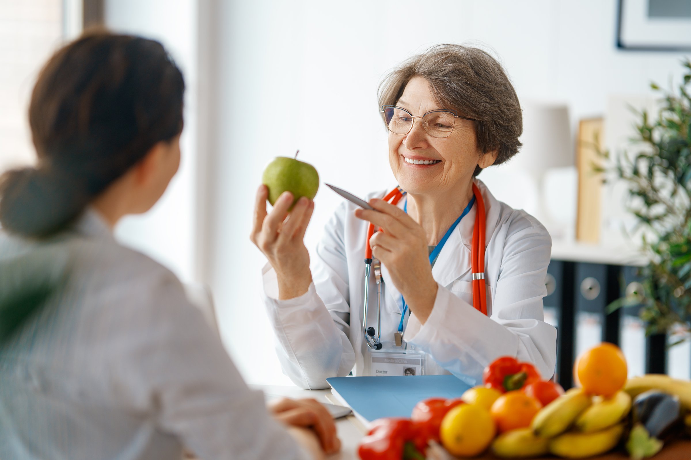 Happy doctor is working in medicine office. A woman is talking to a patient about the importance of eating fruits and vegetables.