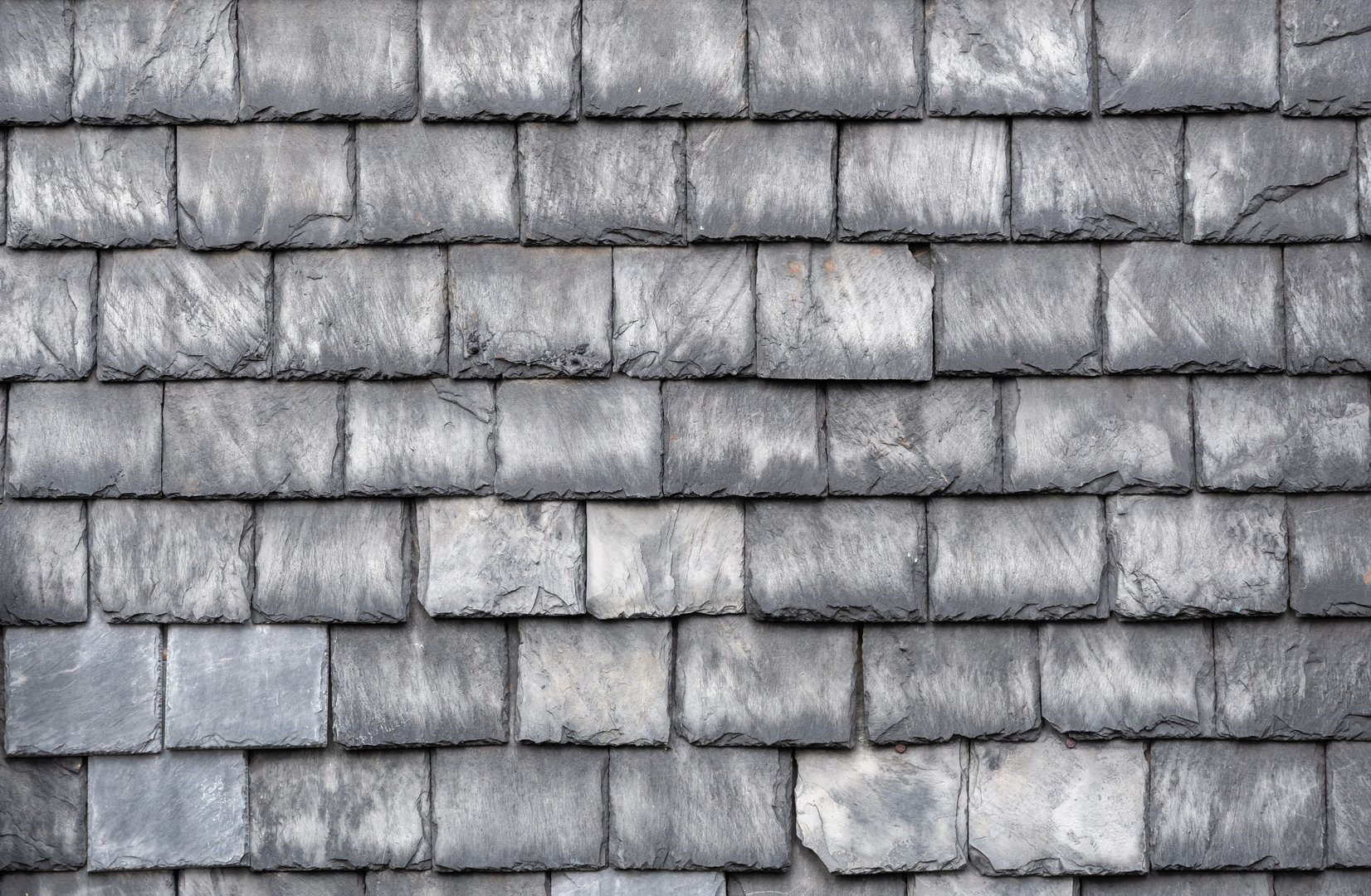 Gray slate roof tiles interlocking tightly, presenting weathered texture and architectural resilience, highlighting traditional roofing craftsmanship with protective surface pattern